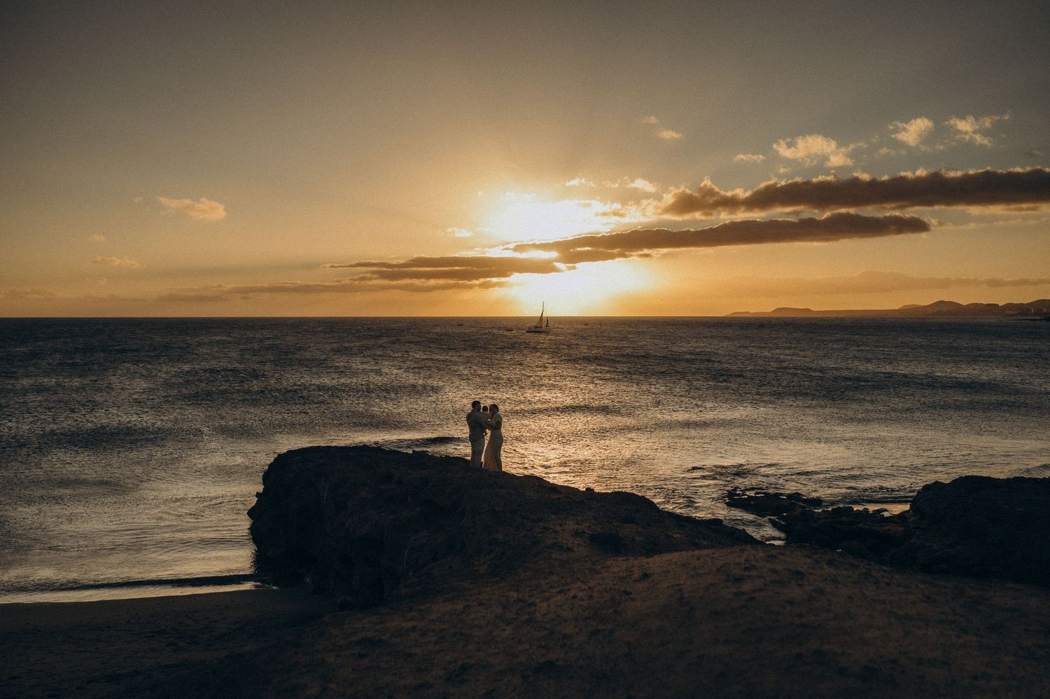 Silhouettes of figures walking on beach at sunset with dramatic orange sky and ocean waves in background.