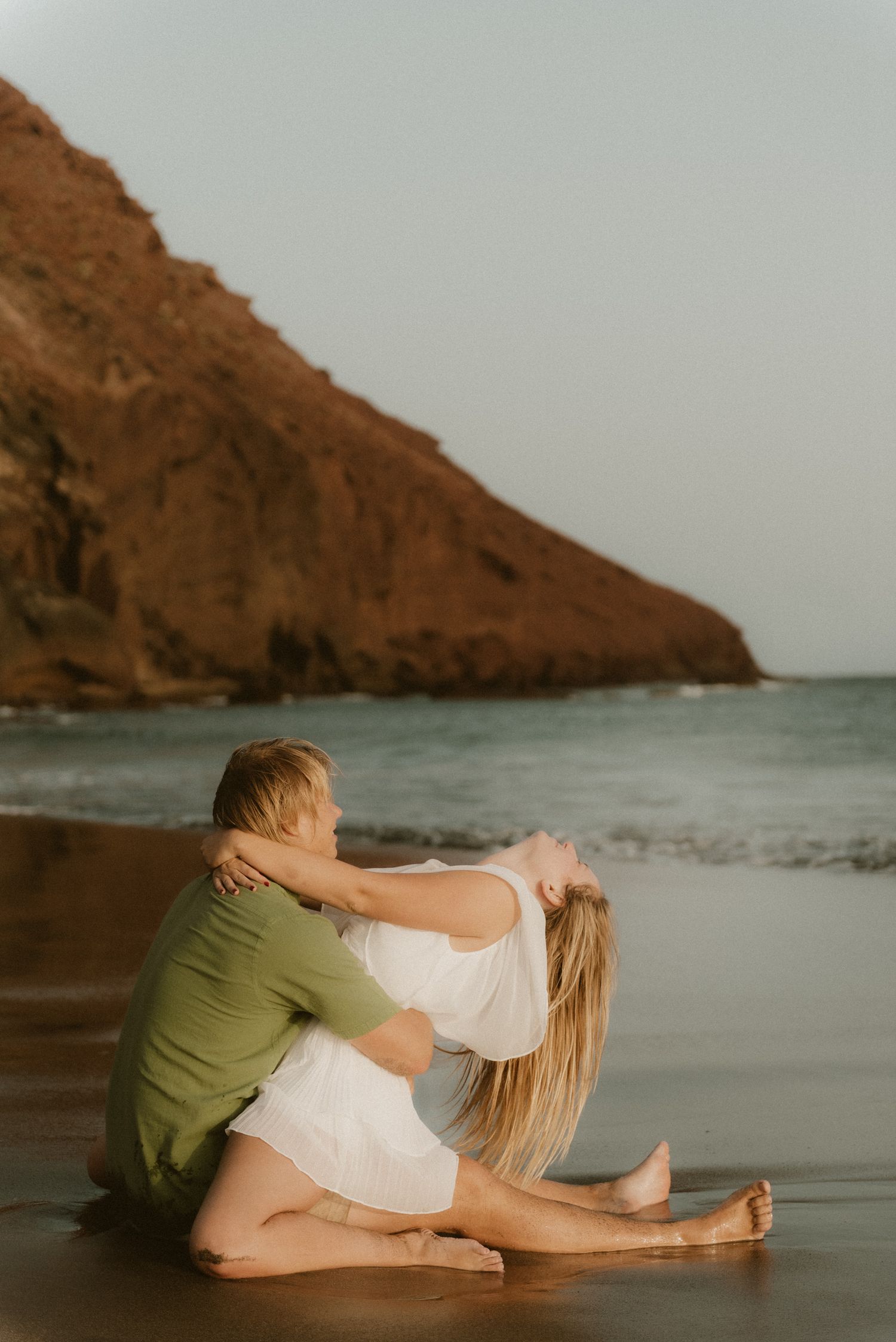 Young couple hugging and enjoying a romantic moment on Playa Tejita with Montaña Roja in the background, Tenerife couples photoshoot