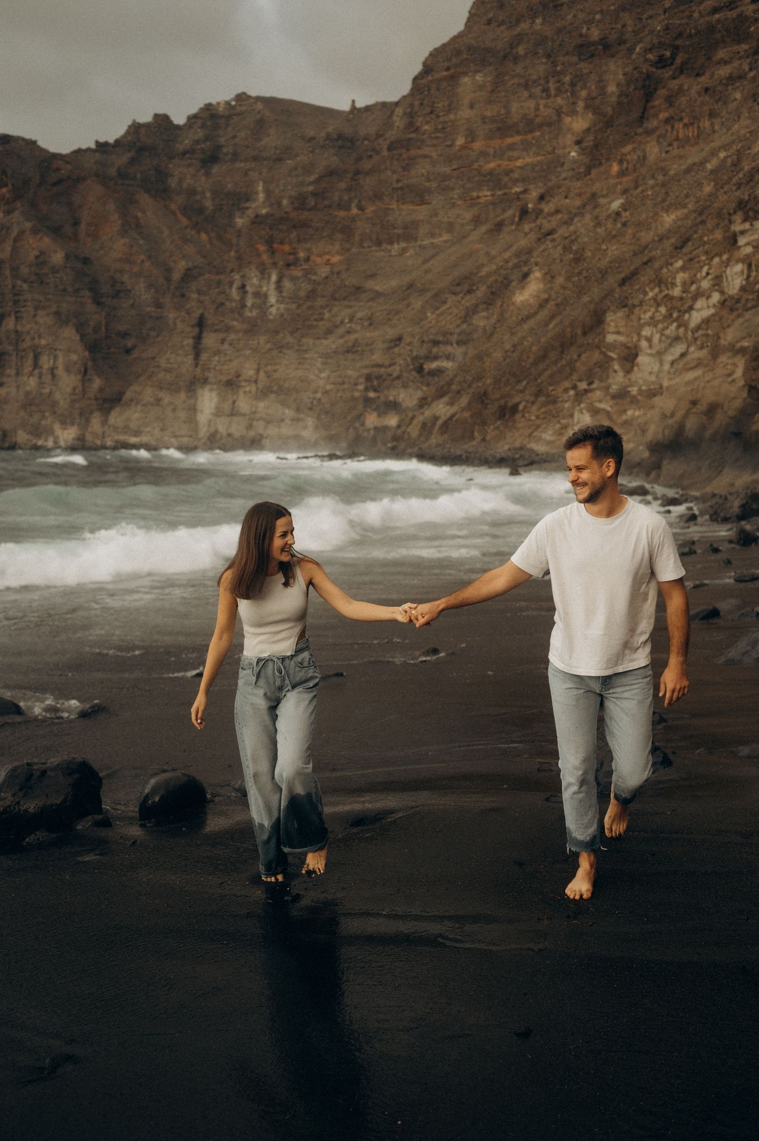 Romantic seaside walk of couple on Playa de Los Guíos beach, Tenerife with cliffs