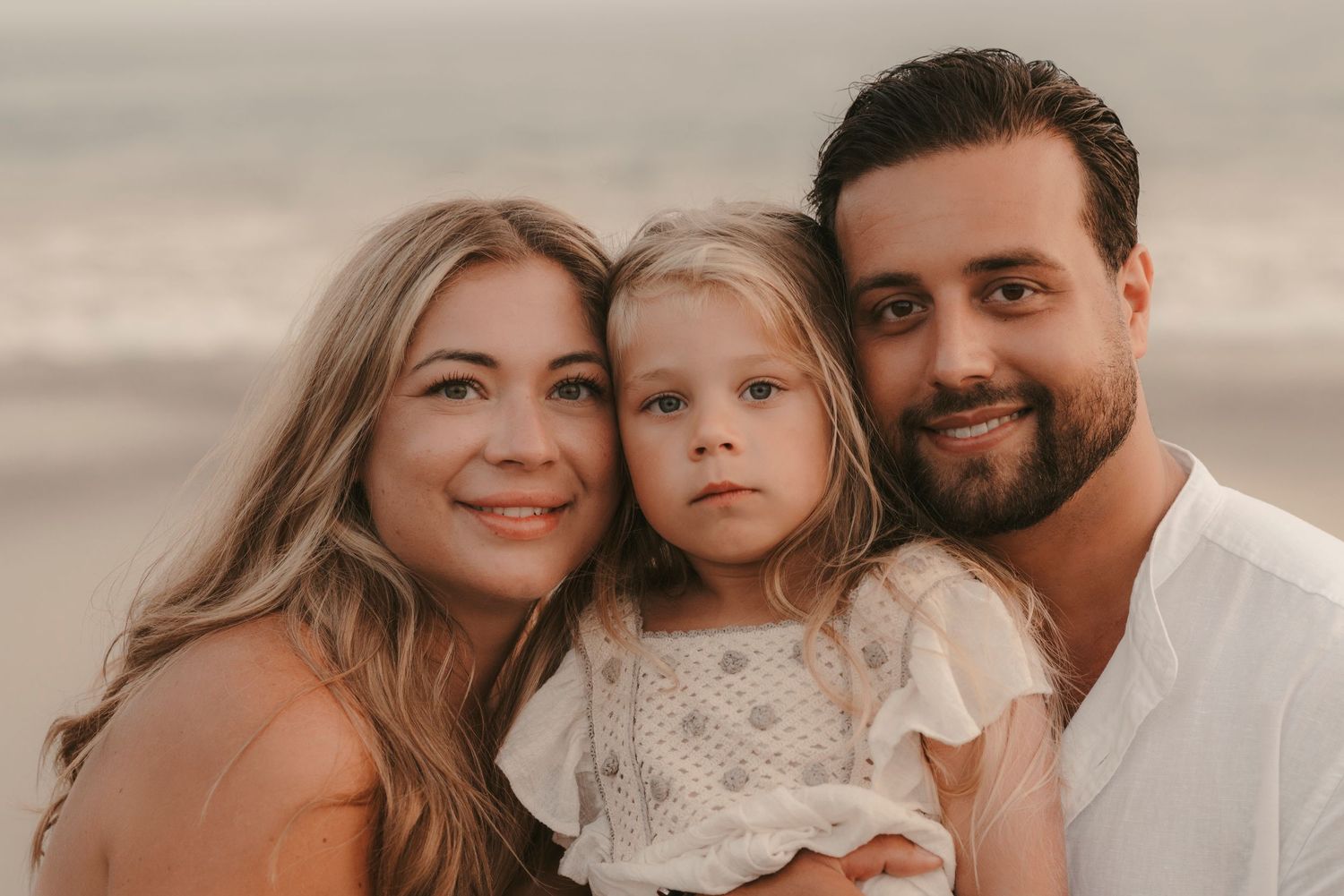 Portrait of a family of three looking at the camera on Playa de la Tejita beach with ocean in the background, Tenerife