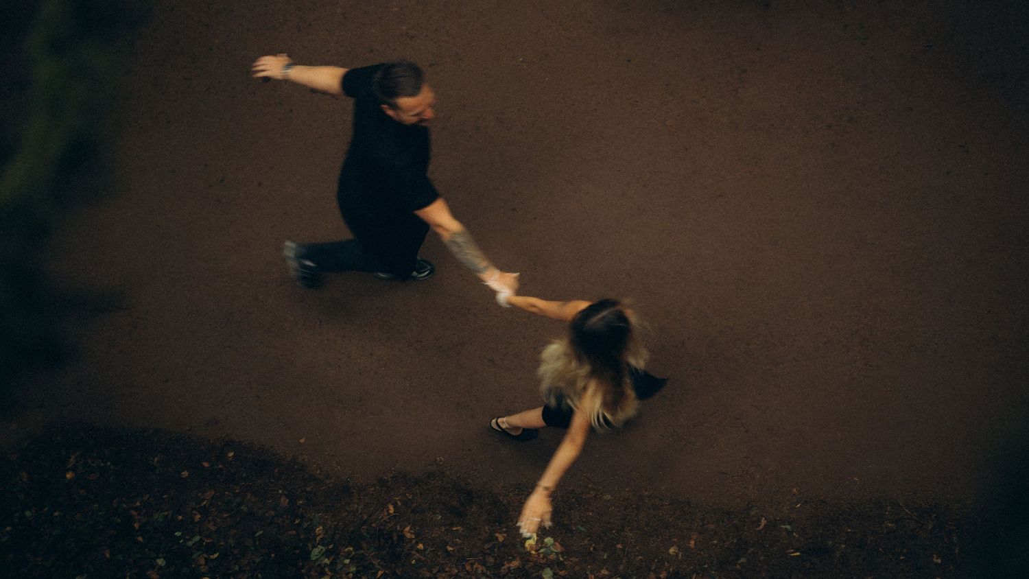Aerial view of a man on a skateboard reaching out to a woman lying on the ground outdoors.