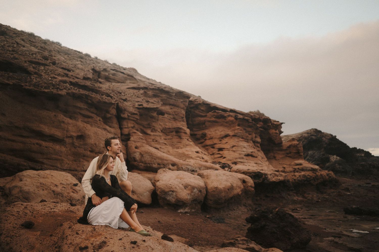 Young couple sitting on cliffs, enjoying the scenic ocean view during a photoshoot in Tenerife