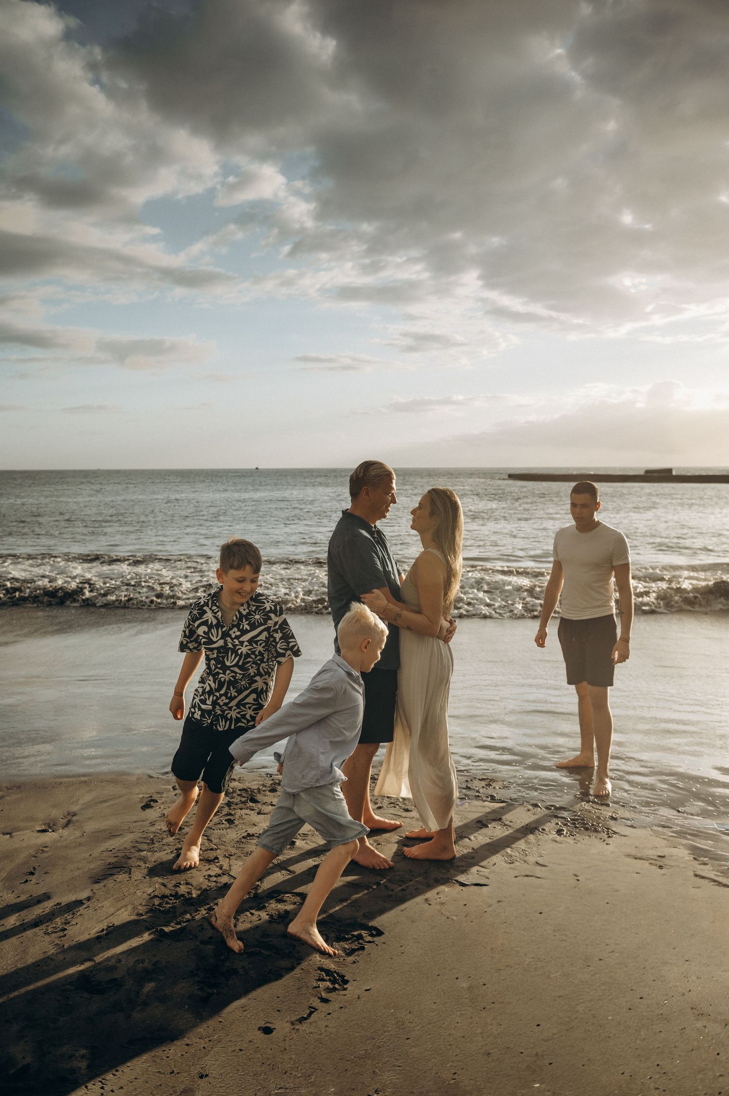 Parents looking into each other’s eyes as children run around them on beach, Playa Fañabé