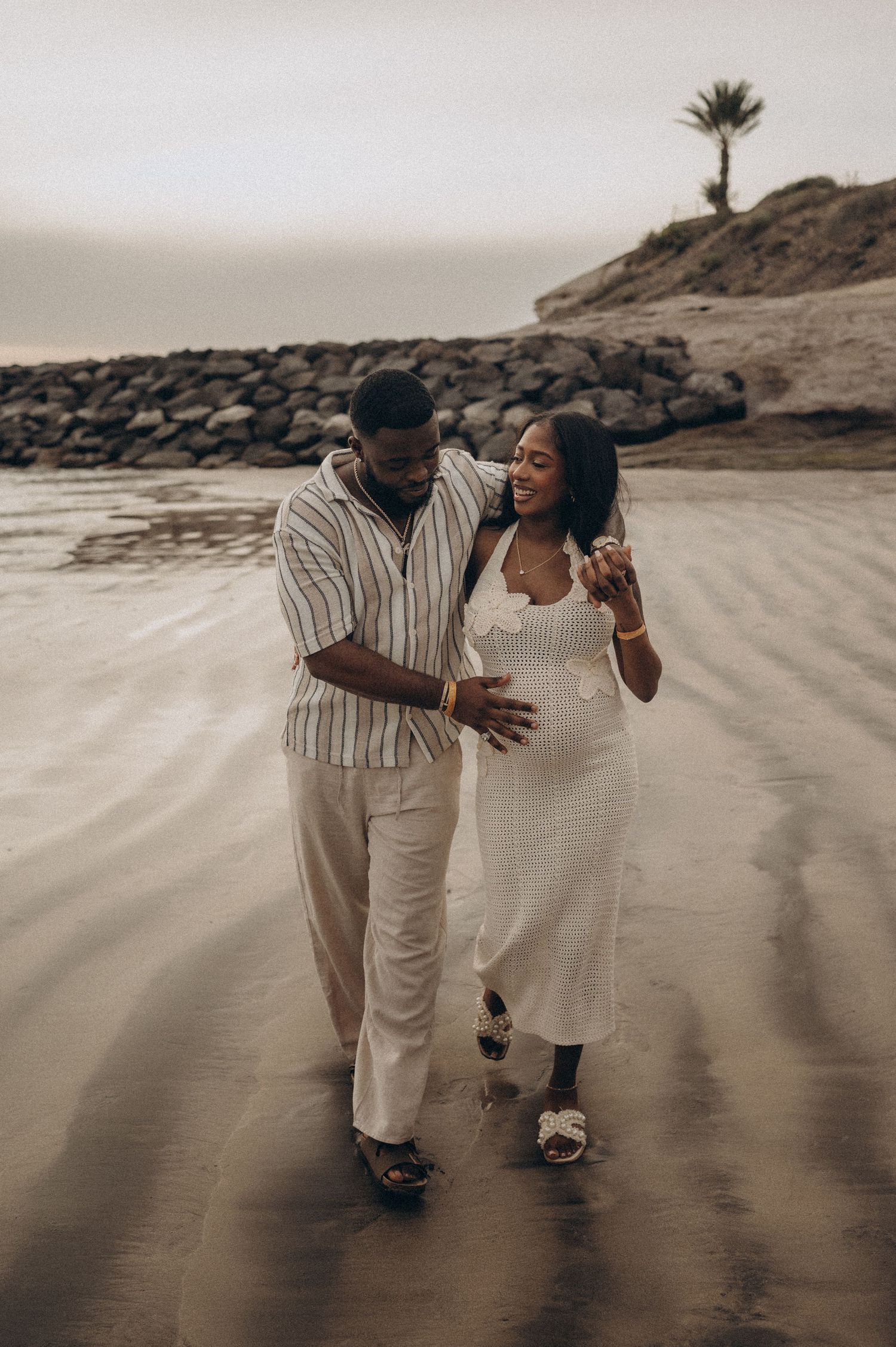 Maternity moment with partner hugging and touching expectant belly on beach, Playa Fañabé