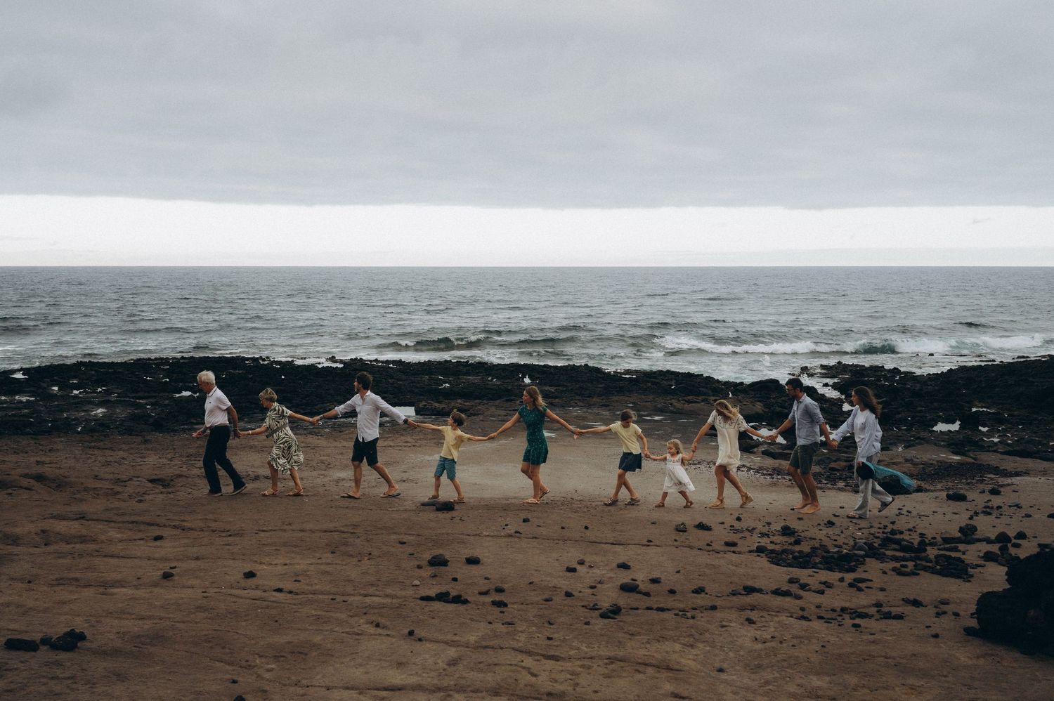 Family forming a line holding hands along rocky coast with ocean and sky in Tenerife