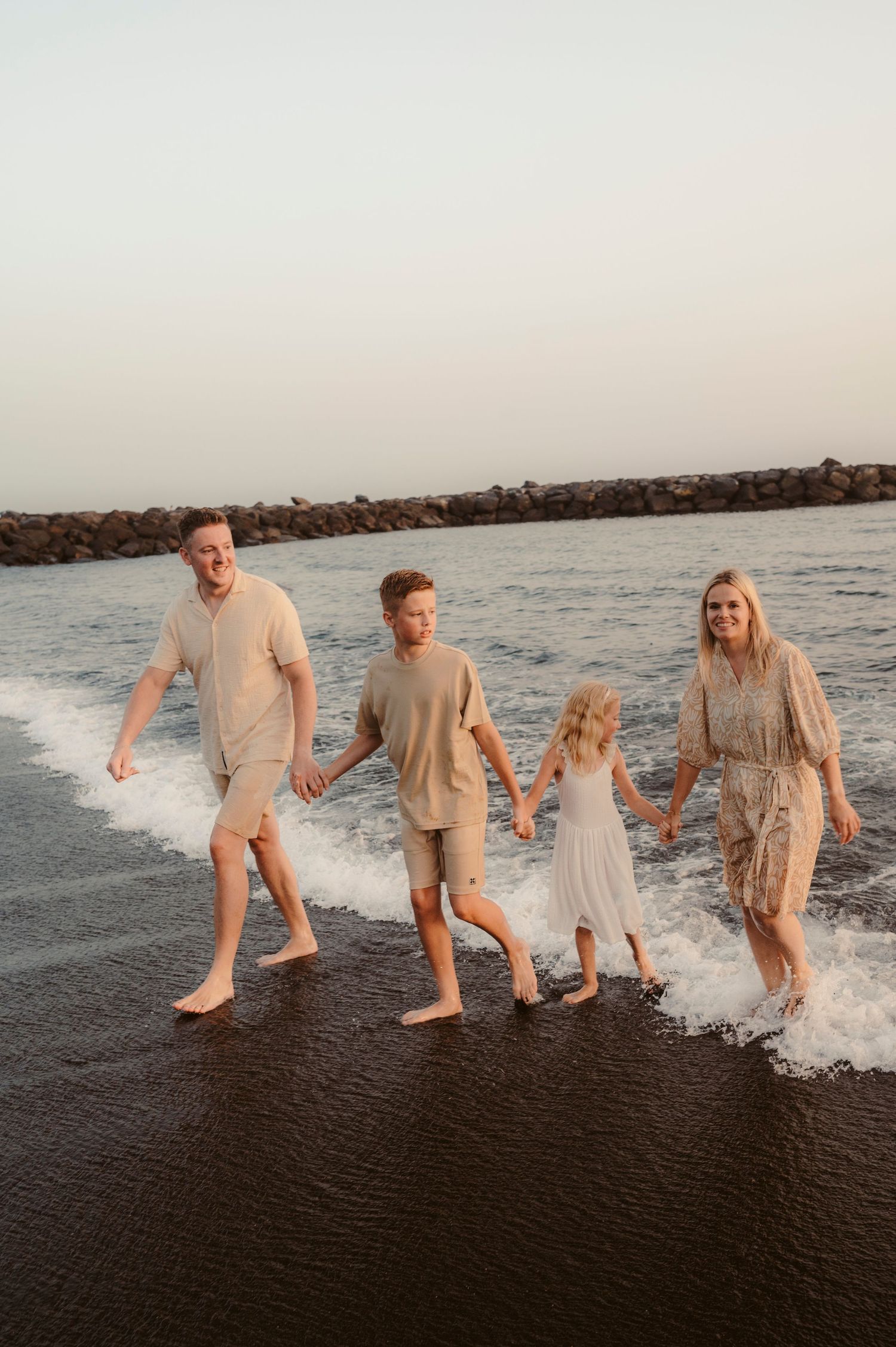 Whole family walking together from ocean onto black sand beach, Playa del Duque
