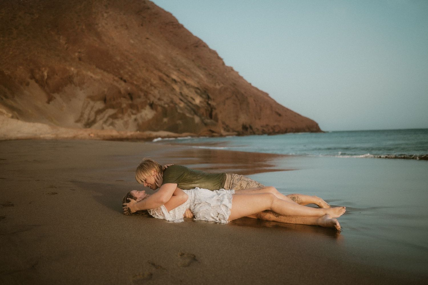 Young couple lying on the sand, bride’s dress flowing, capturing romantic moments at Playa Tejita