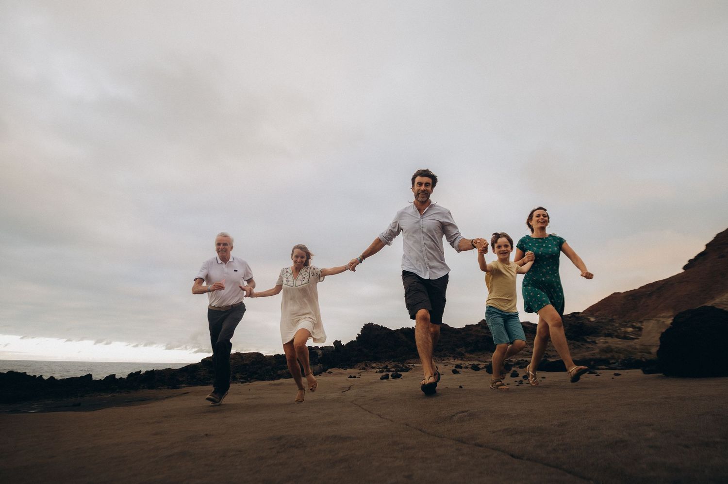Group of five family members running toward camera along rocky coastline in Tenerife