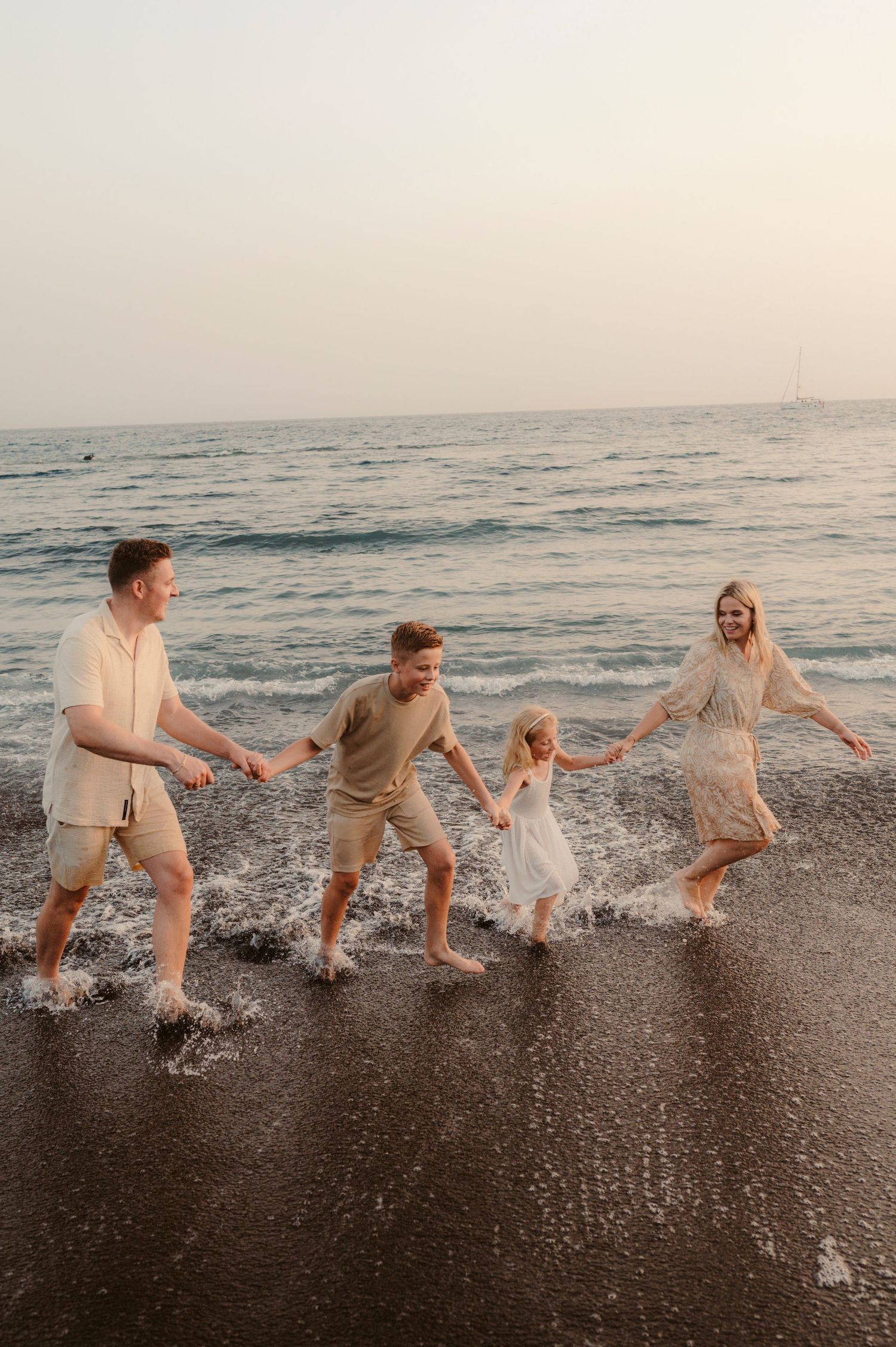 Family running hand in hand along ocean at sunset, Playa del Duque