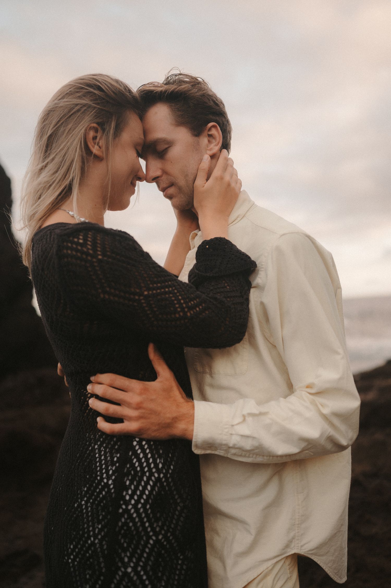 Romantic close-up of a young couple gazing at each other, with ocean and cliffs behind them, Tenerife photoshoot