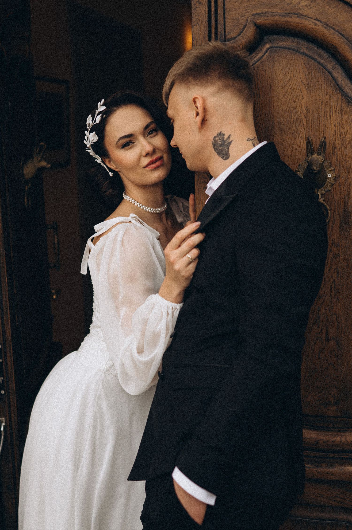 Elegant bride posing for the camera while the groom admires her closely during their wedding photoshoot.