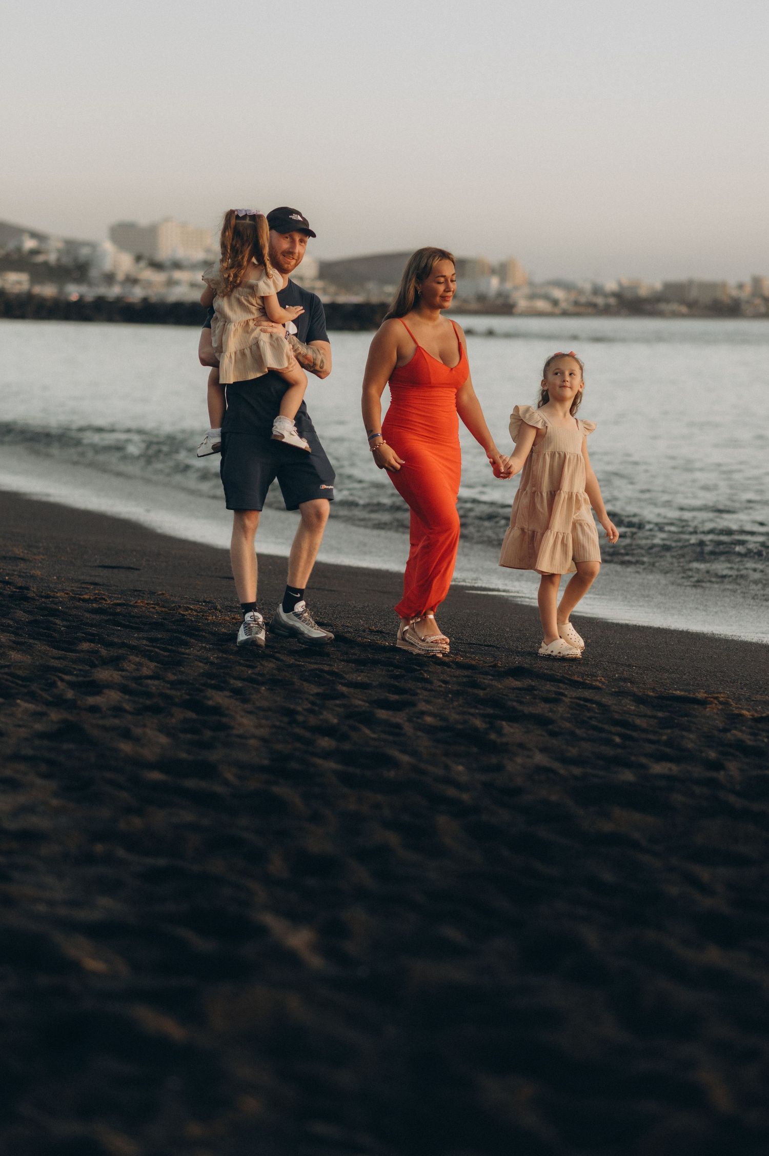 Parents and their two daughters walking together on Playa del Duque beach at sunset