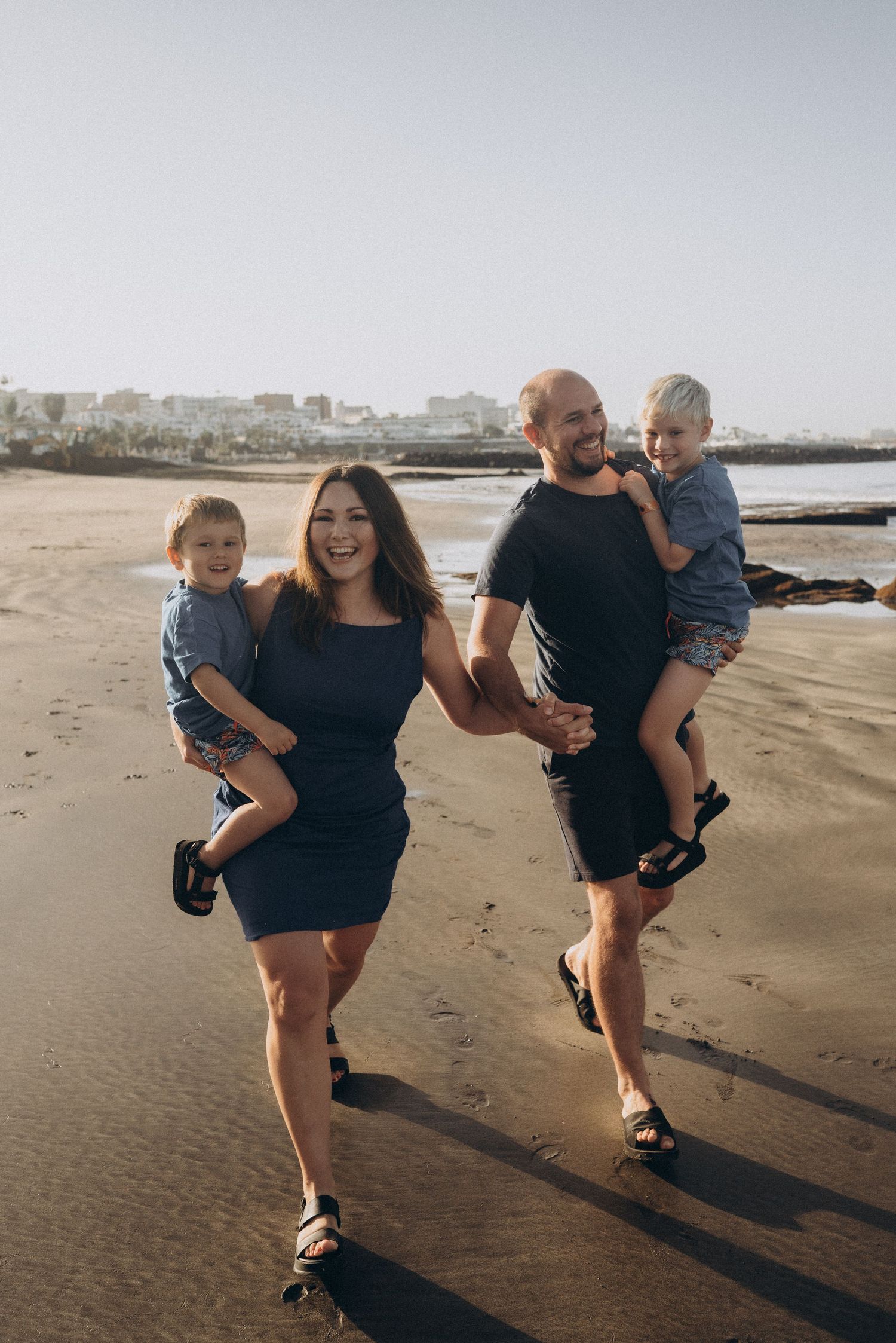 Loving family scene with parents holding hands and sons snuggled against them at Playa Fañabé