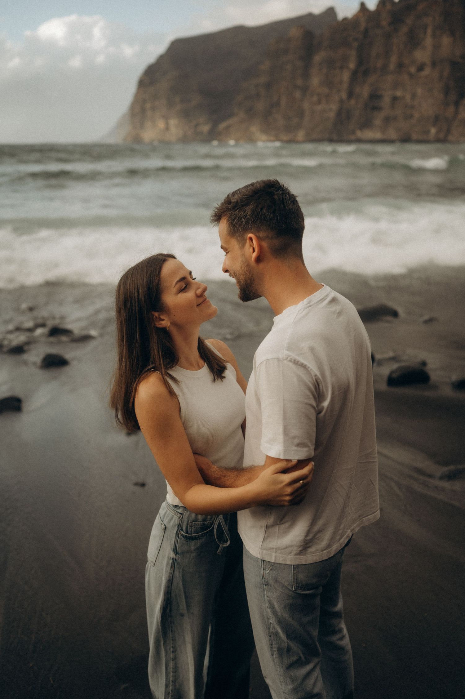 Young couple hand-in-hand walking along Playa de Los Guíos, Tenerife cliffs behind