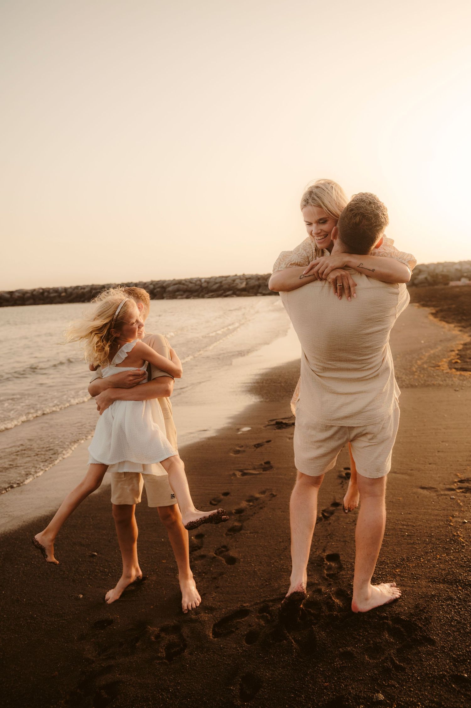 Parents and children laughing and playing on volcanic sand at sunset, Tenerife