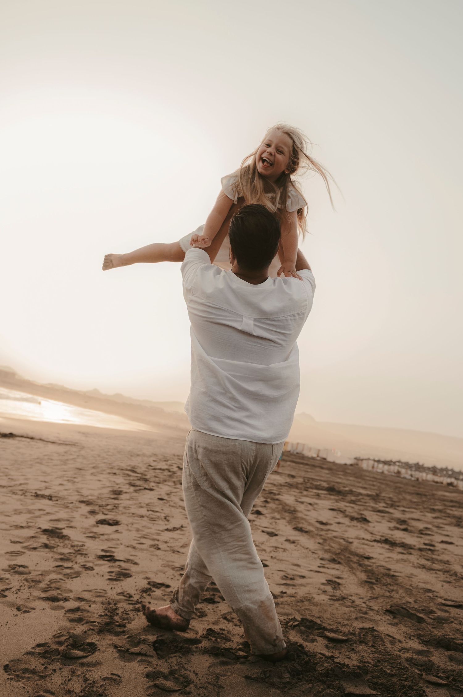 Smiling father and daughter captured in playful lift on the beach at Playa La Tejita