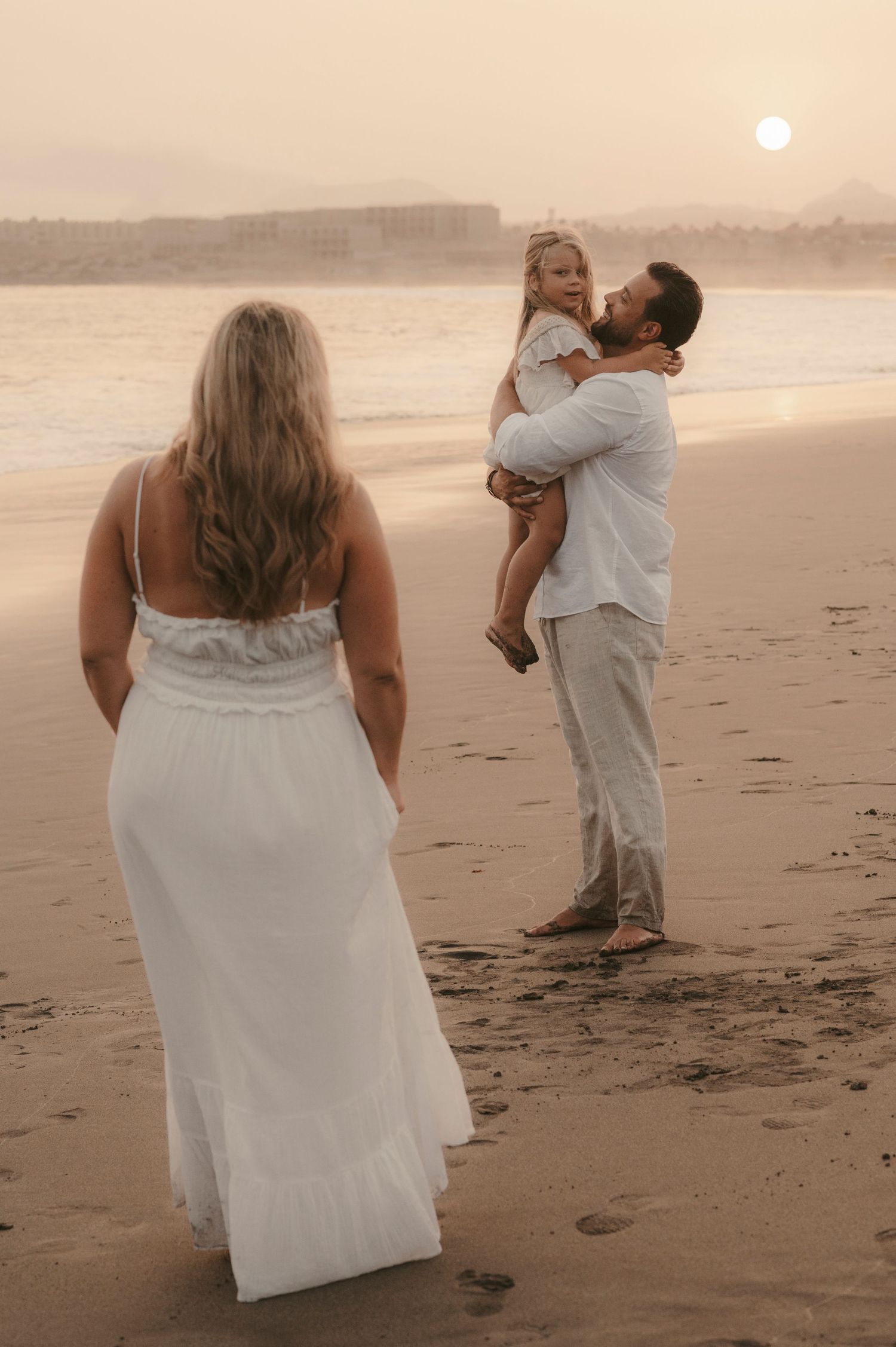 Mother watching from a distance as father holds their daughter enjoying the sunset at Playa La Tejita