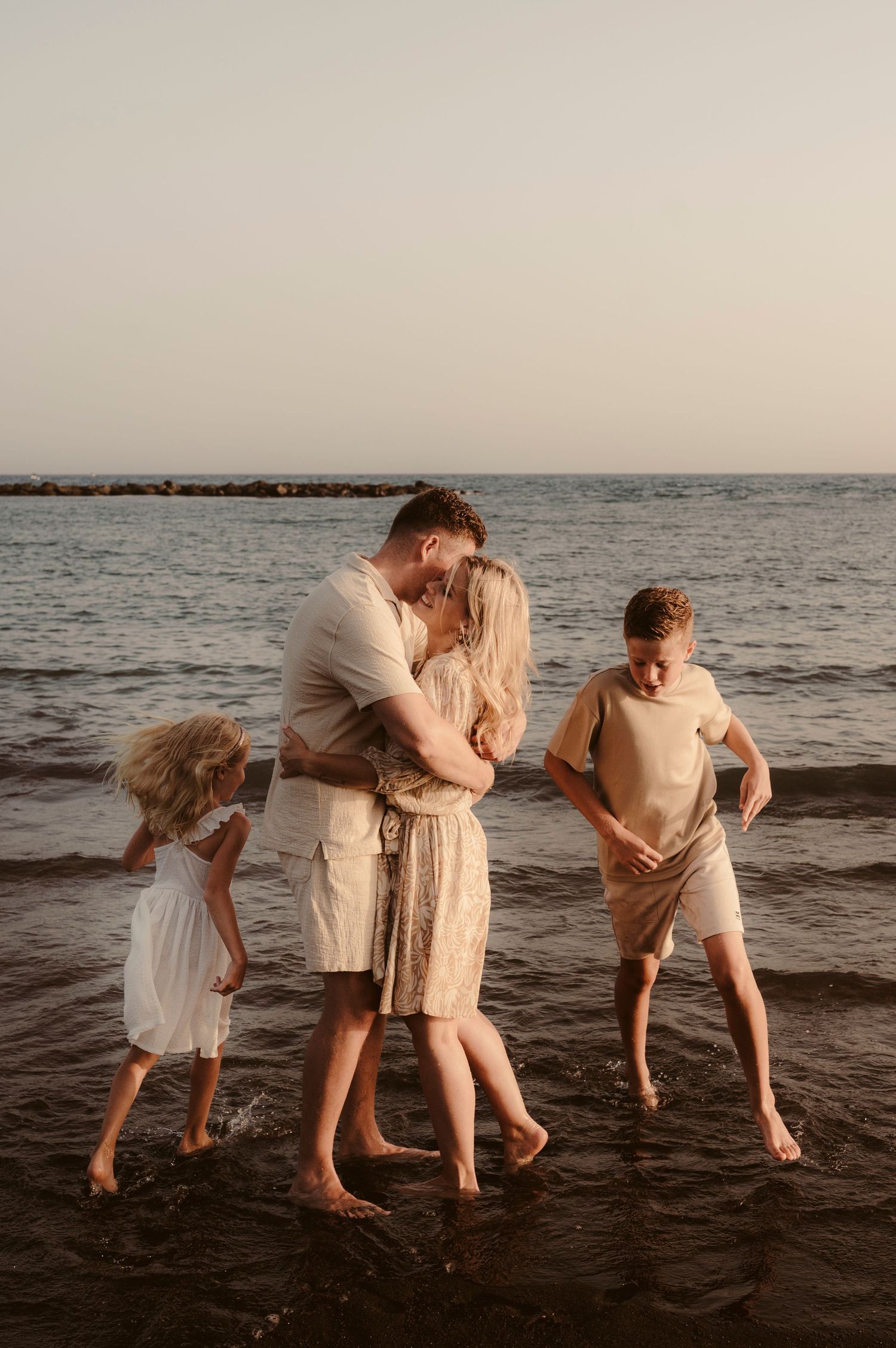 Children running around parents embracing each other at sunset, Playa del Duque