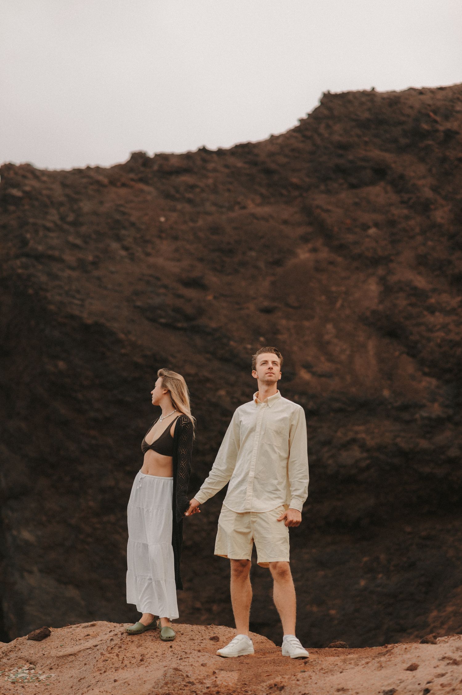 Couple standing side by side, holding hands with majestic cliffs in the background under Montaña Roja, Tenerife