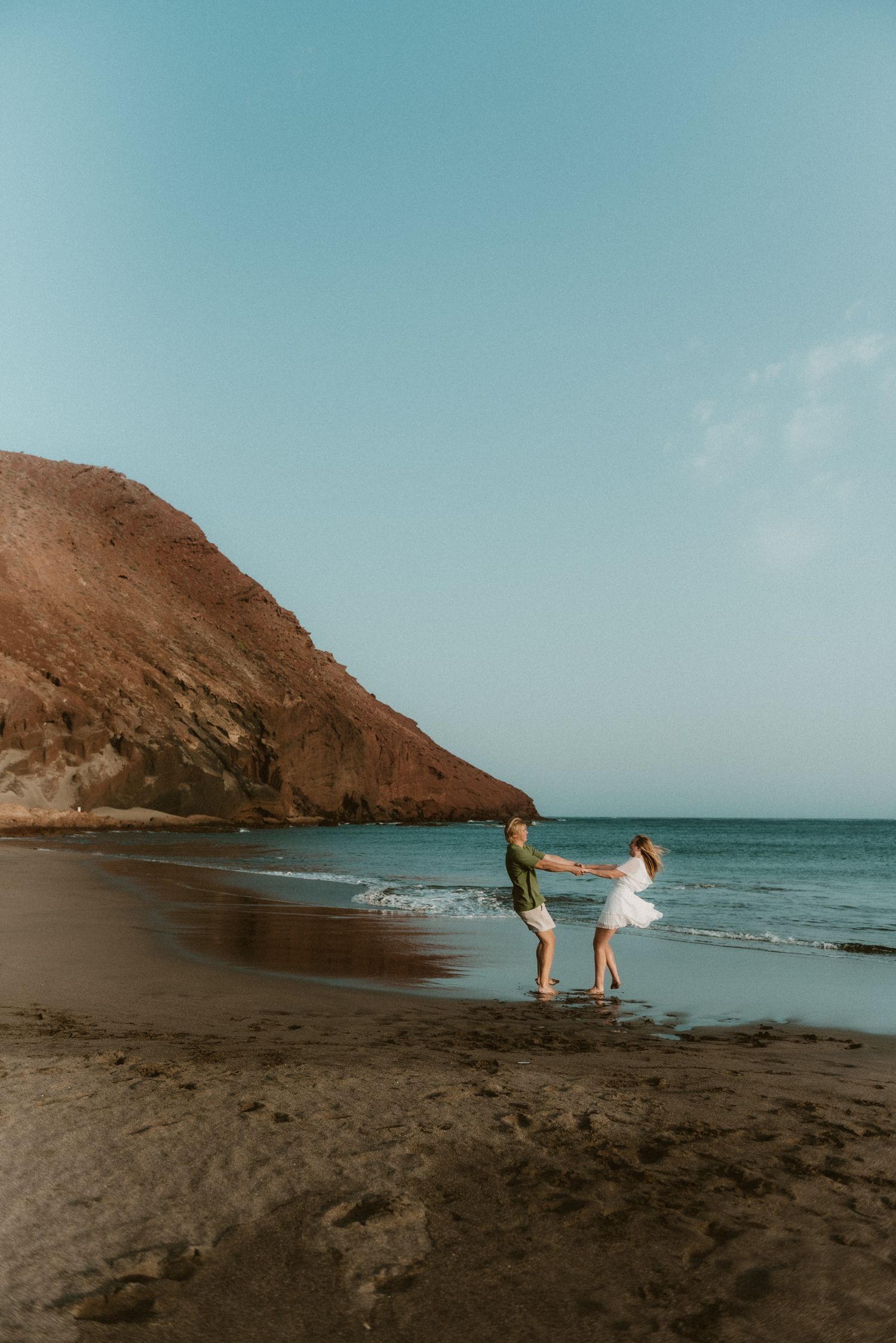 Young couple dancing in the middle of Playa Tejita with Montaña Roja in the distance and beautiful ocean, Tenerife couples photoshoot