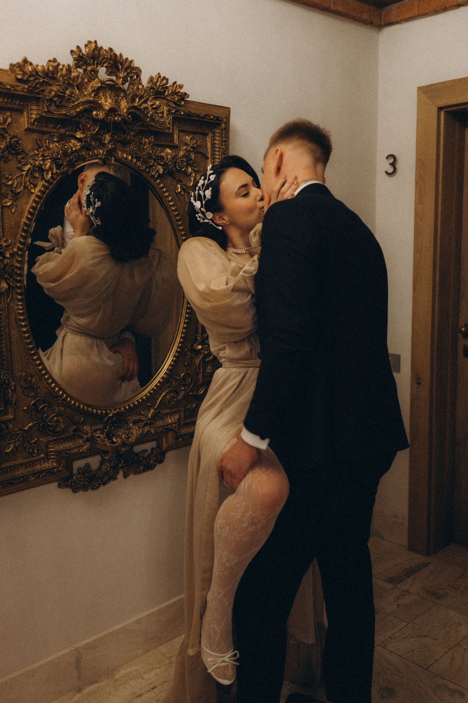 Bride and groom sharing an intimate moment as he kisses her neck while she leans against a wall during their wedding photoshoot.