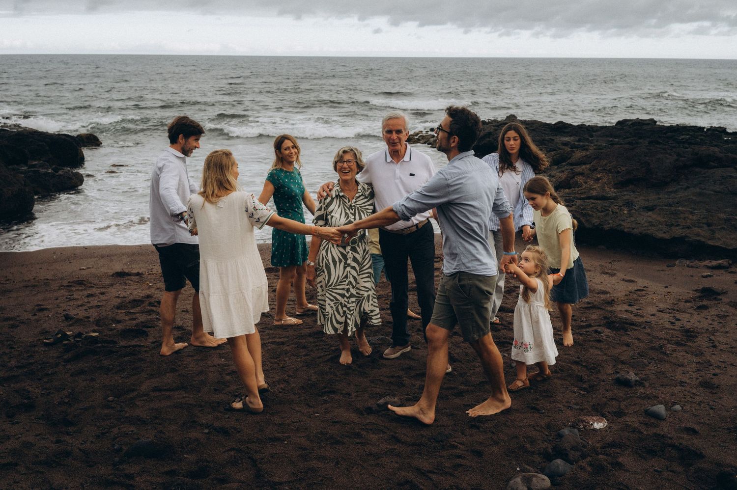 Elderly couple in center of joyful family circle holding hands on black sand at Los Refugios