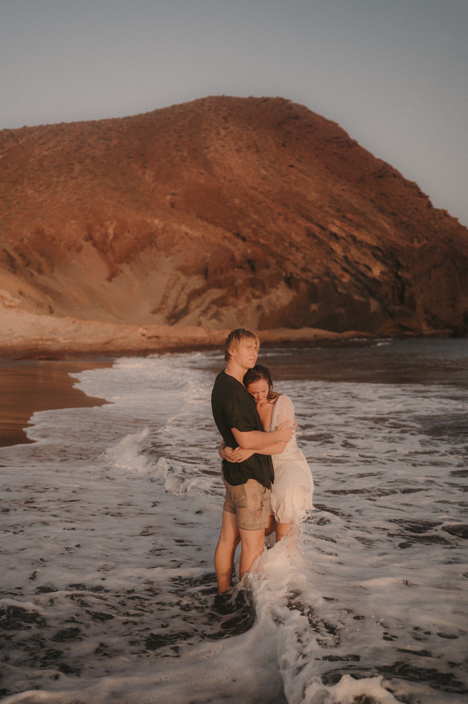 Couple holding hands on Playa Tejita with Montaña Roja and ocean in the background, Tenerife couples photoshoot