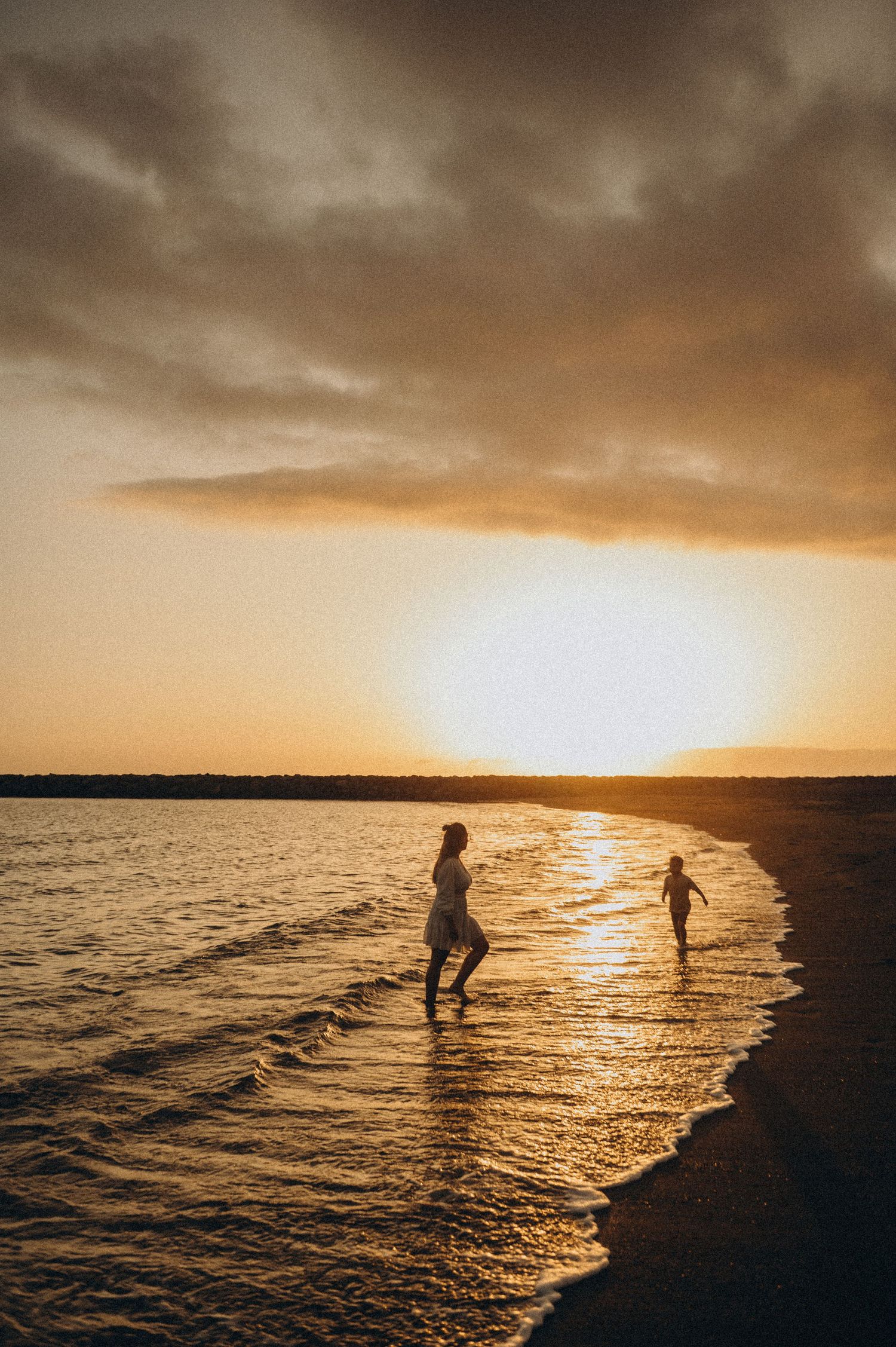 Mother playing with son by sea at sunset on Playa del Duque Tenerife