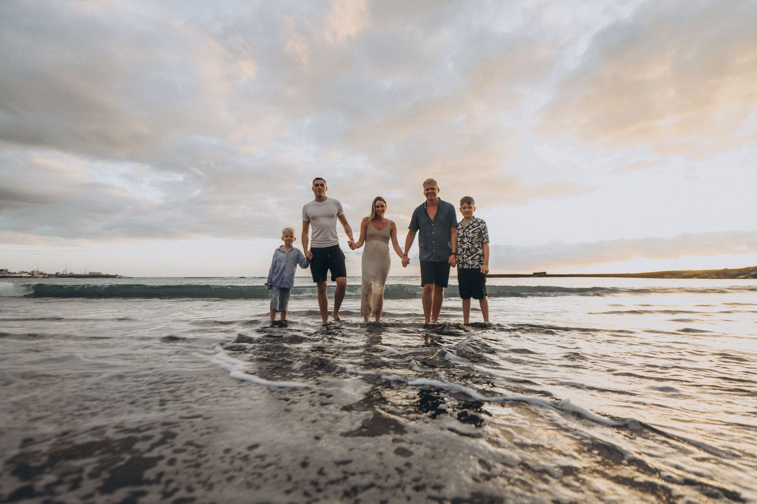 Family walking hand in hand in shallow water at sunset with pink sky, Tenerife