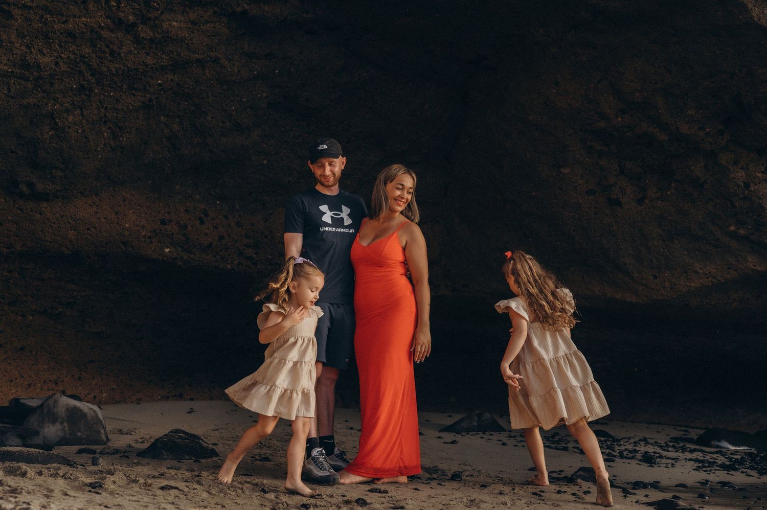 Daughters running around parents standing under a cliff cave on Tenerife beach