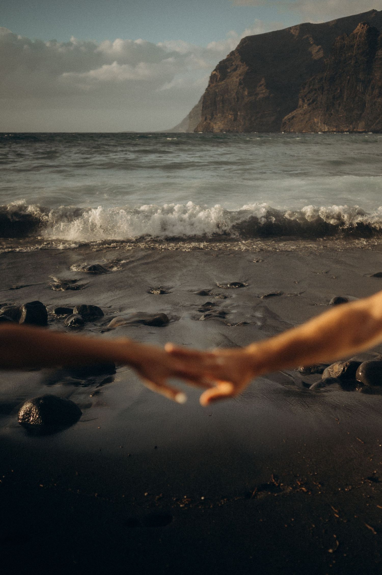 Romantic close-up of couple holding hands on Playa de Los Guíos, Tenerife cliffs