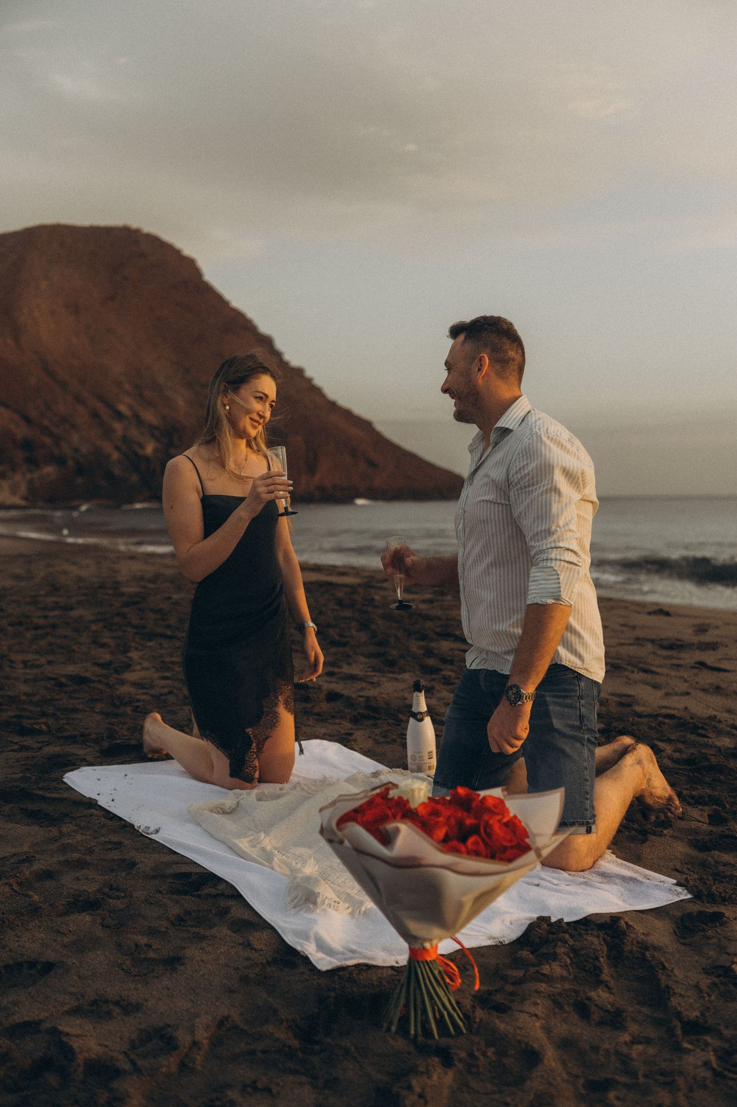 Couple celebrating engagement with roses and champagne on Playa de La Tejita beach, Tenerife
