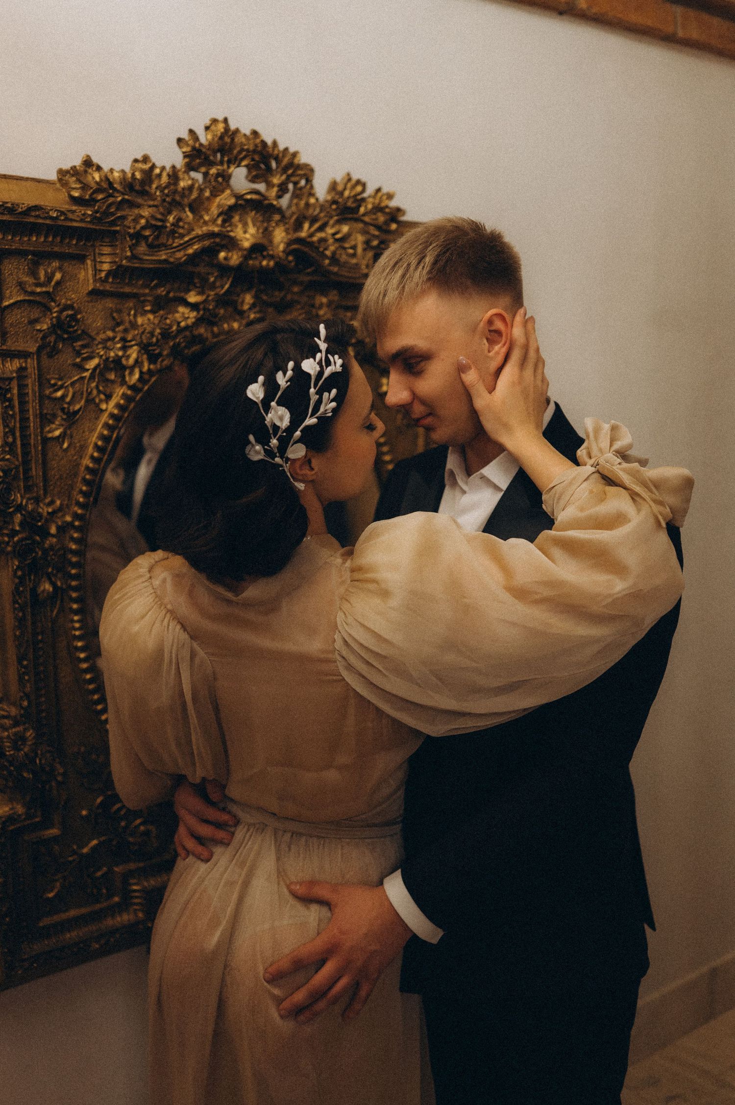 Bride gently touching the groom's face as they look at each other in a mirror during their wedding photoshoot.