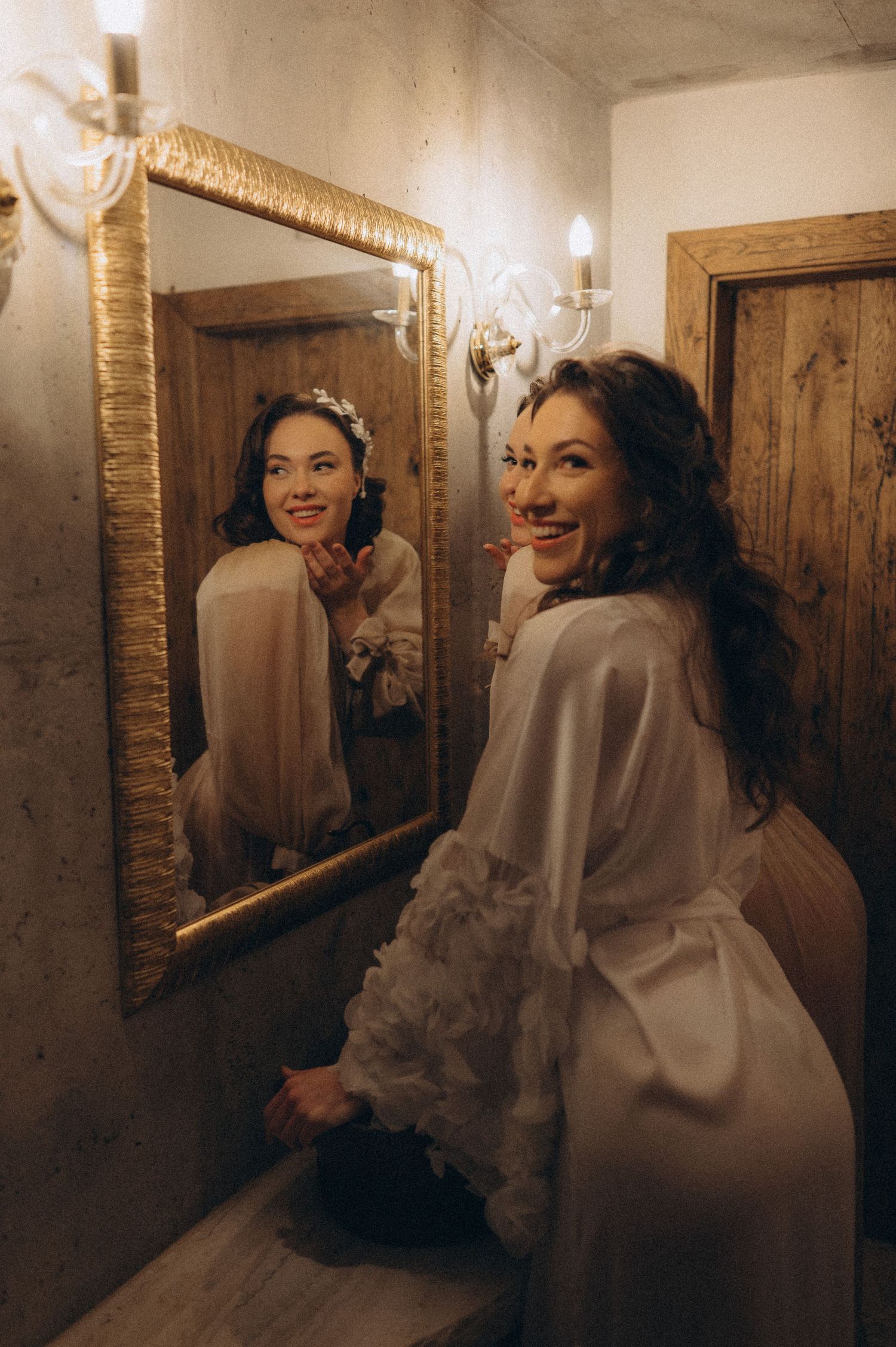 Elegant bridal portrait of the bride posing in front of a gold-framed mirror with her reflection visible.