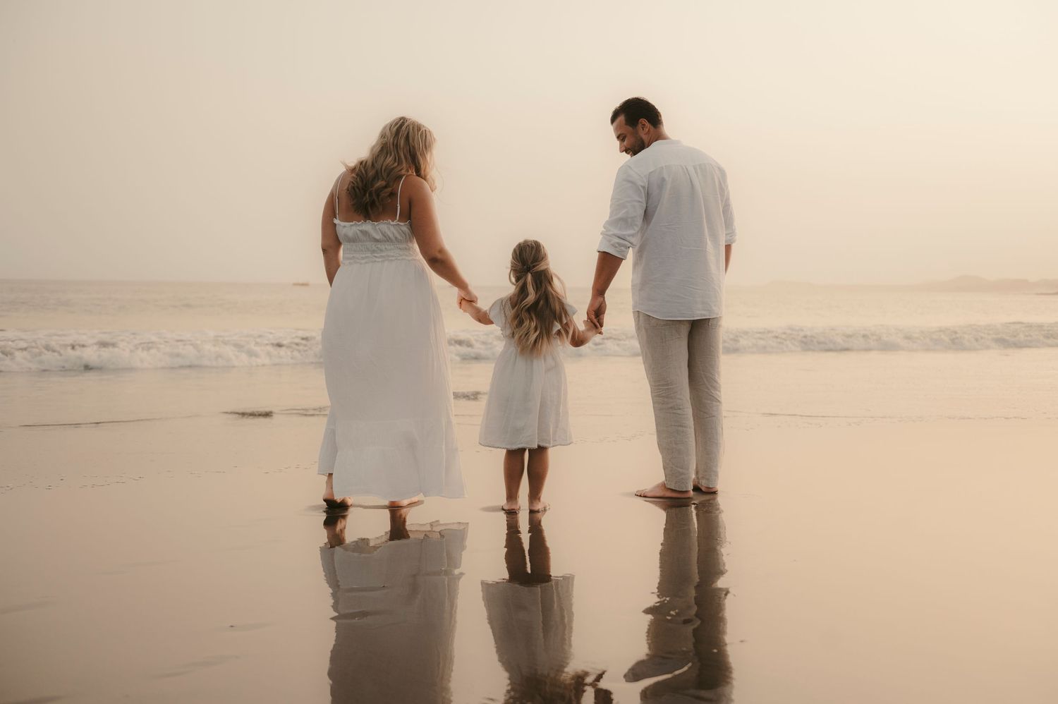 Parents holding their daughter on beach at sunset with perfect reflection in wet sand, Playa la Tejita