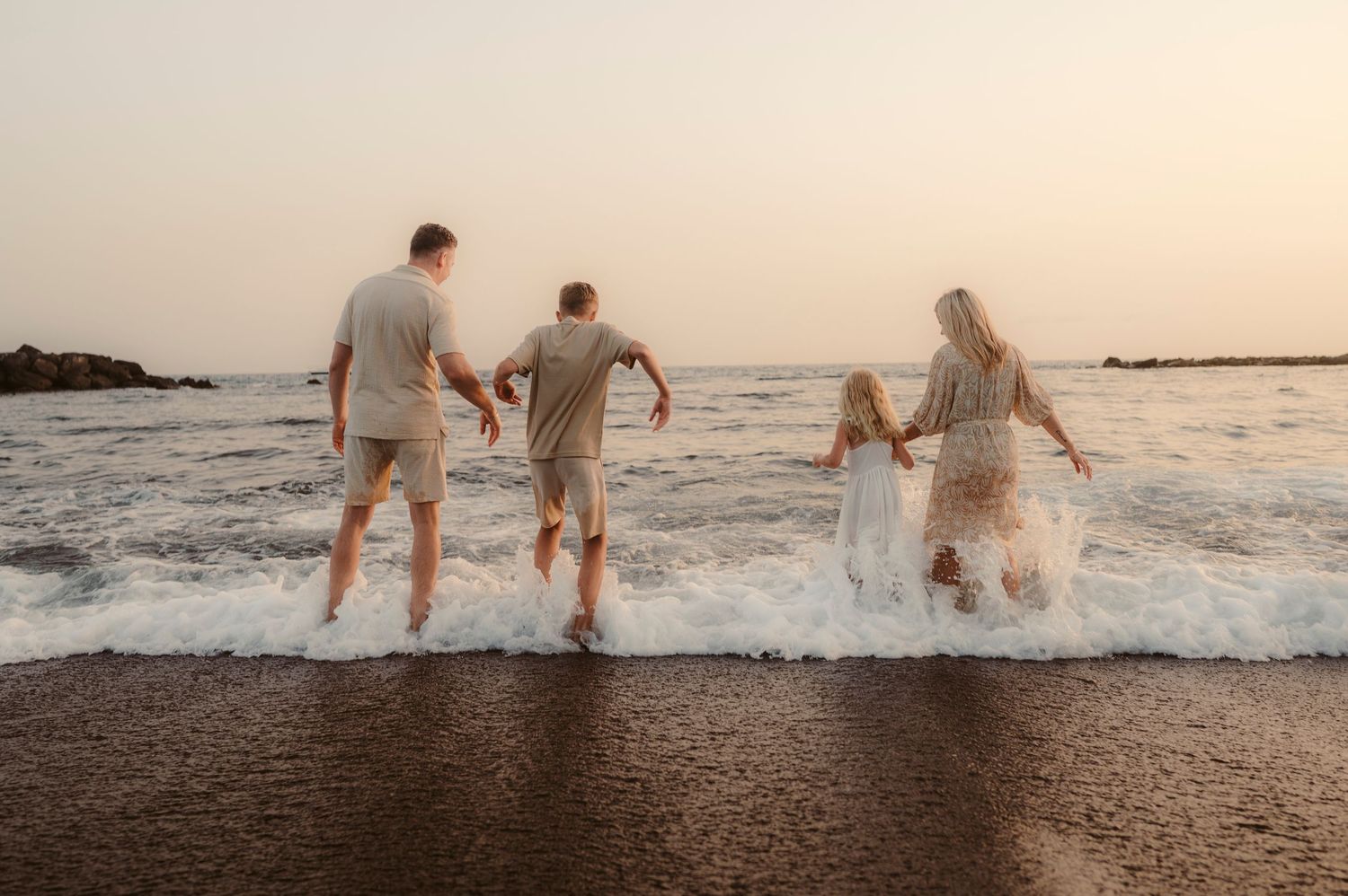 amily running together into ocean waves with black sand and blue-white contrast at sunset, Tenerife