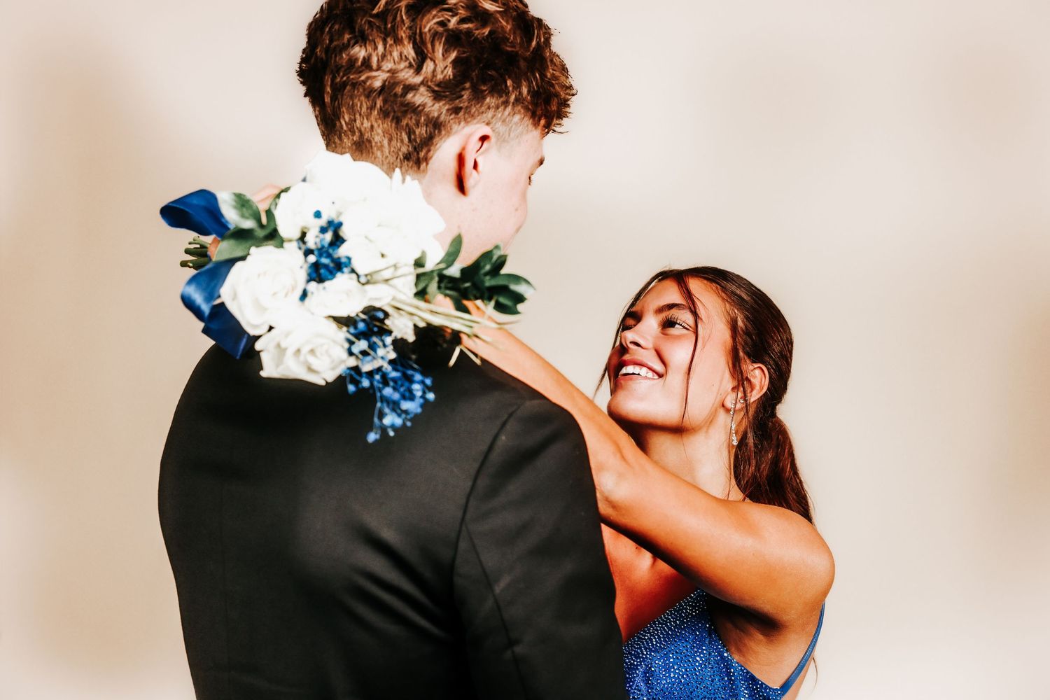 A couple shares romantic embrace and kiss outdoors with blue floral bouquet during intimate wedding photo session.