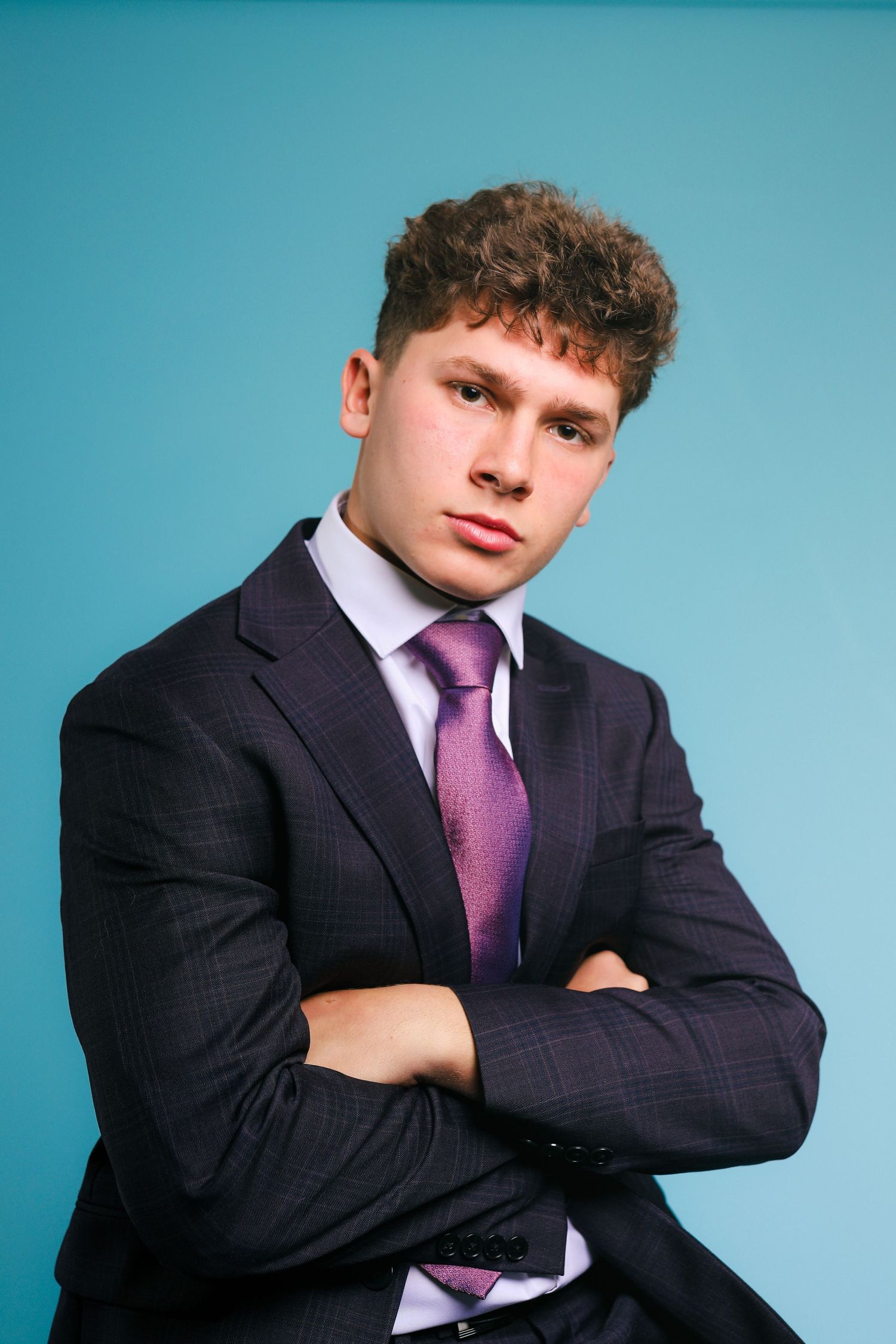 Professional business portrait on turquoise background showing formal attire with navy suit and purple tie.