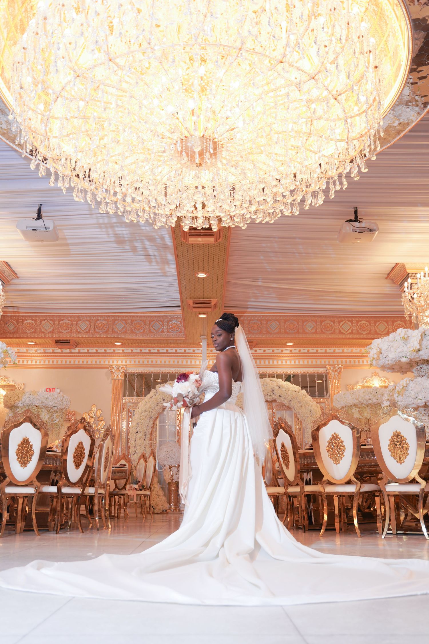 Dramatic bridal portrait under crystal chandelier in luxurious white ballroom setting.