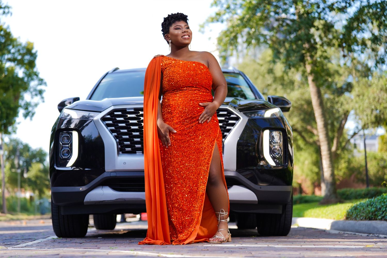 Glamorous photoshoot featuring a sparkling orange evening gown next to a luxury car outdoors in Tampa Florida.