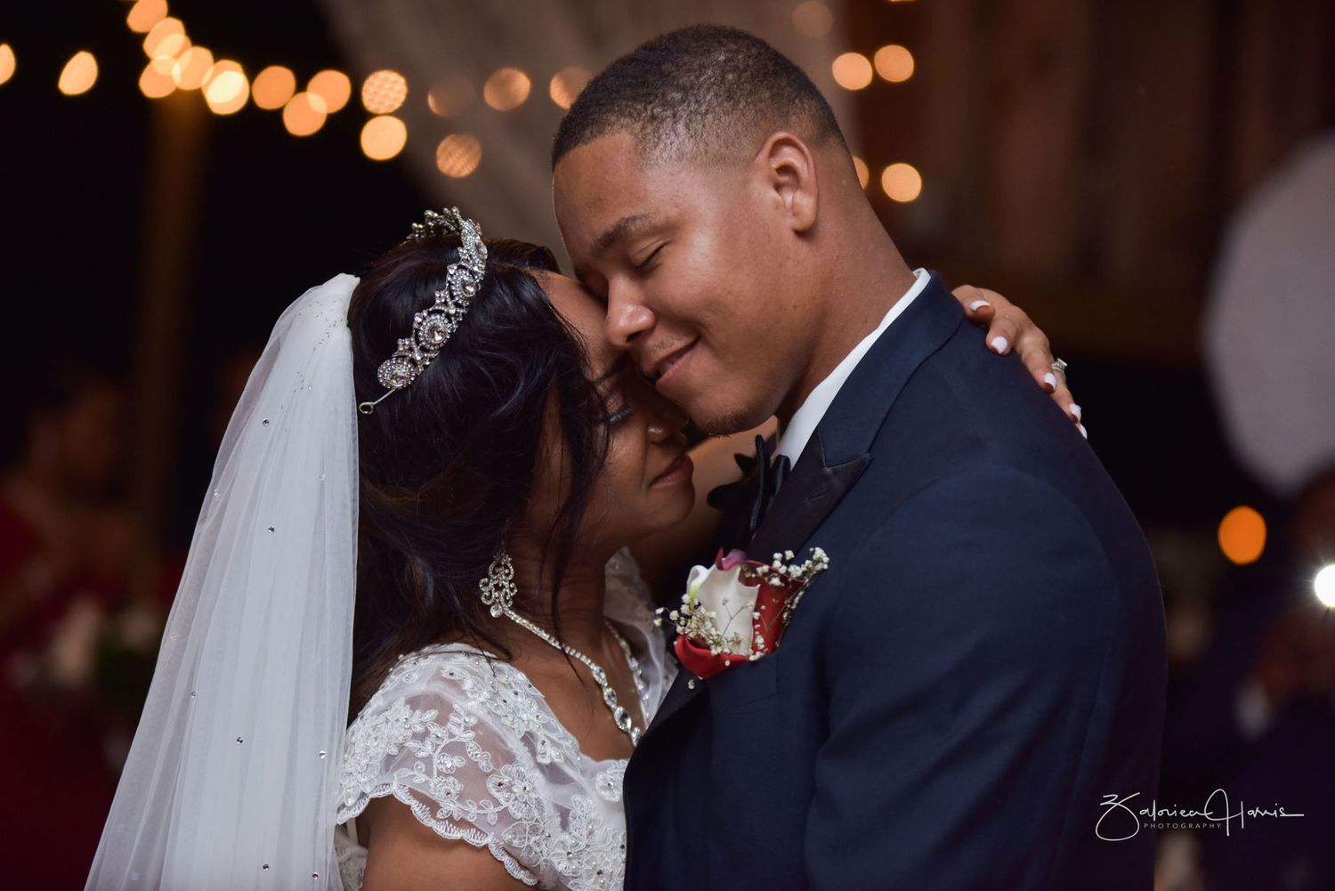 A romantic wedding couple shares intimate moments in a dimly lit venue with bokeh lights in the background.