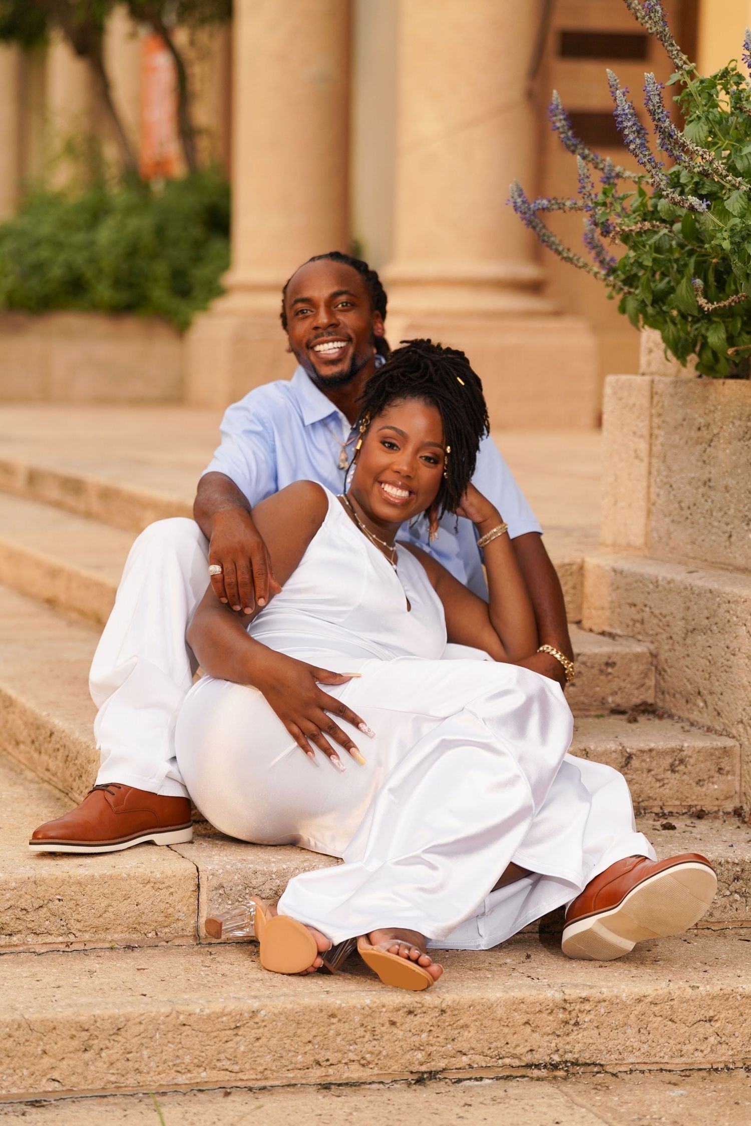 Romantic couple's photoshoot in white outfits on stone steps outdoors.