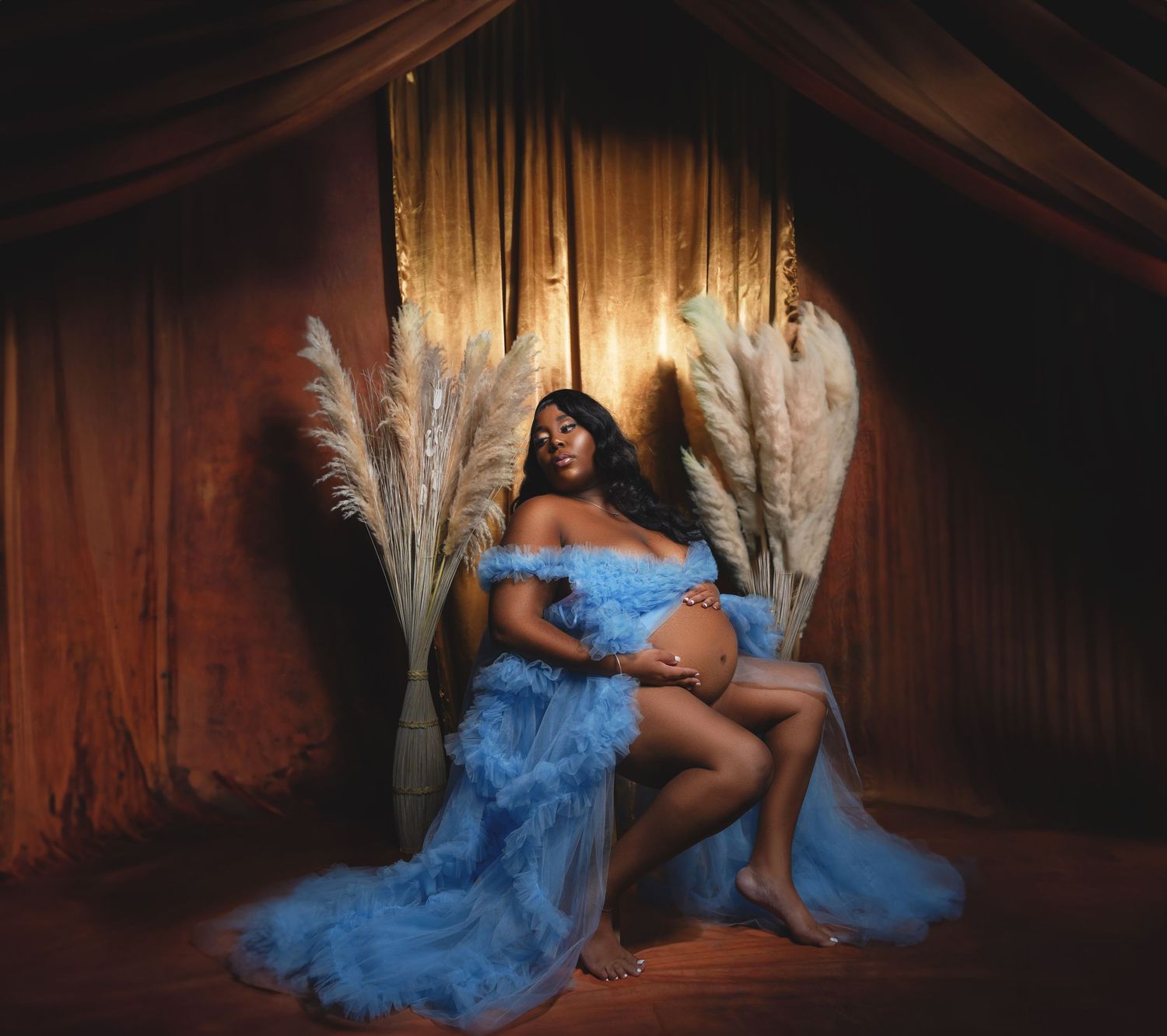 Ethereal maternity photos featuring flowing blue dress in wooden setting with dramatic lighting.