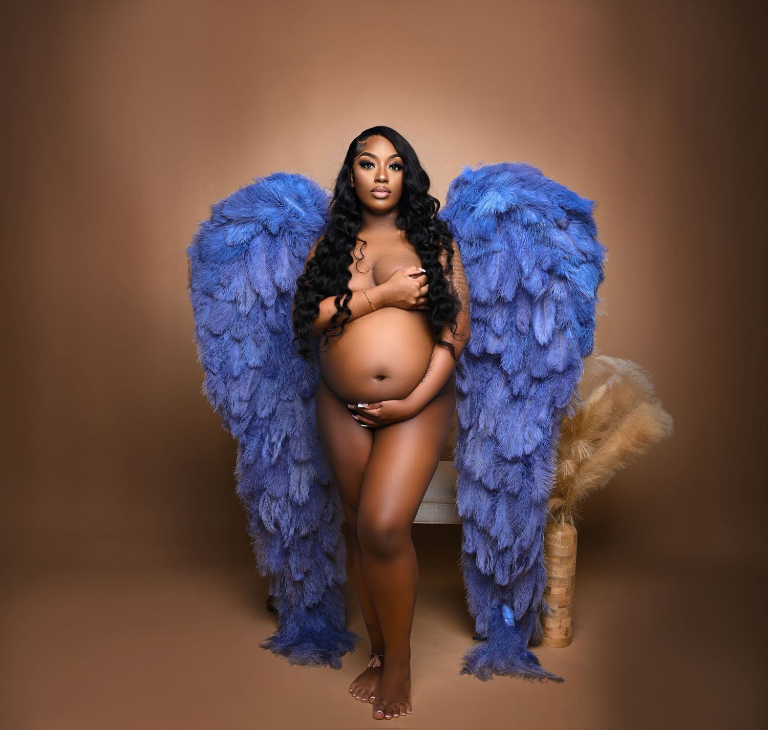 Tampa Florida Artistic maternity portrait with blue feather wings against neutral brown background.