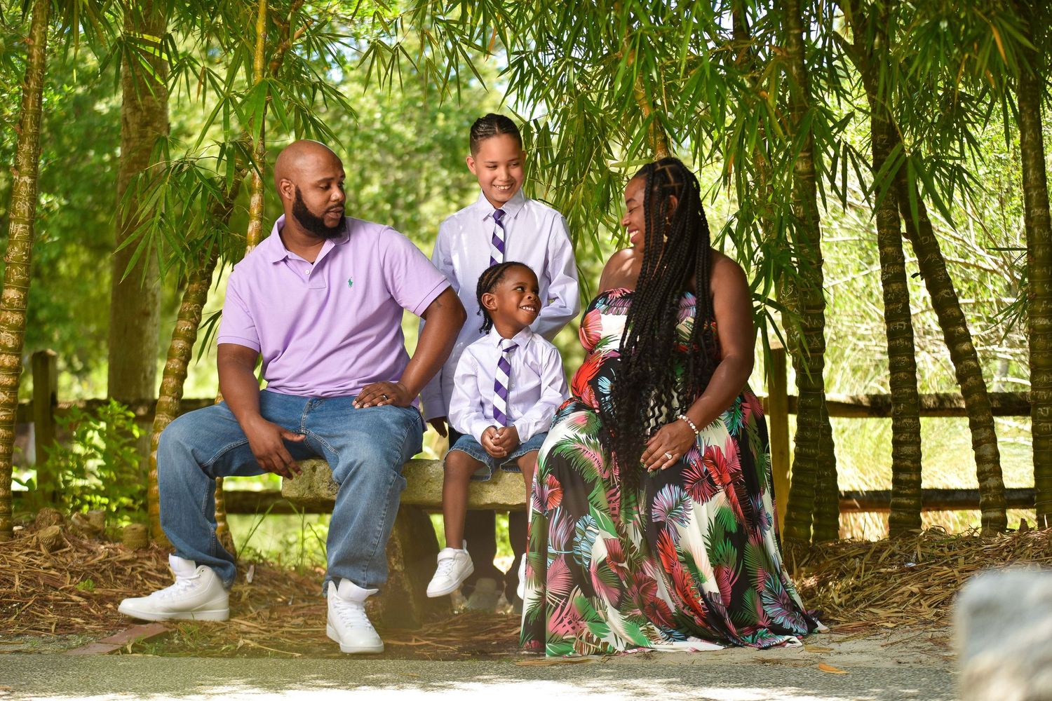 Family of four poses outdoors on bench surrounded by lush green bamboo trees in a park setting.
