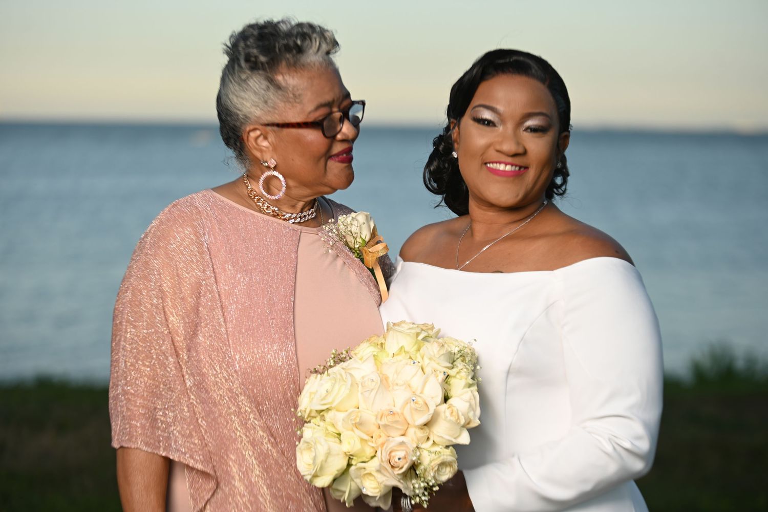 Wedding couple embracing at sunset on a beach with yellow flowers.