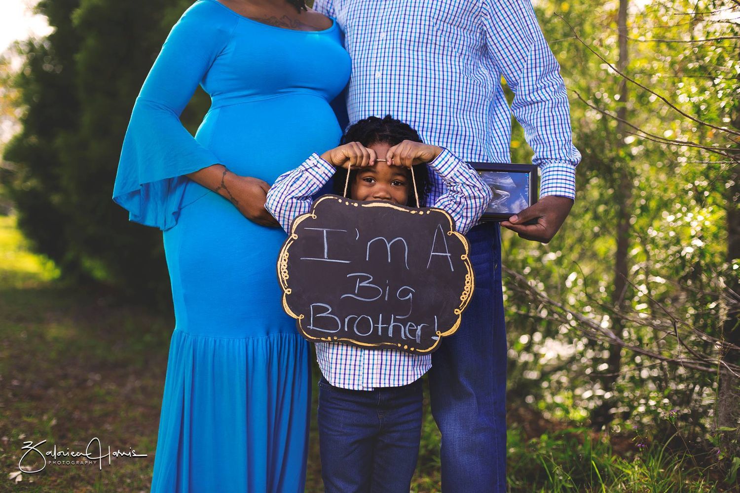 Maternity photo series showing couple outdoors with chalkboard signs and blue dress in natural setting.