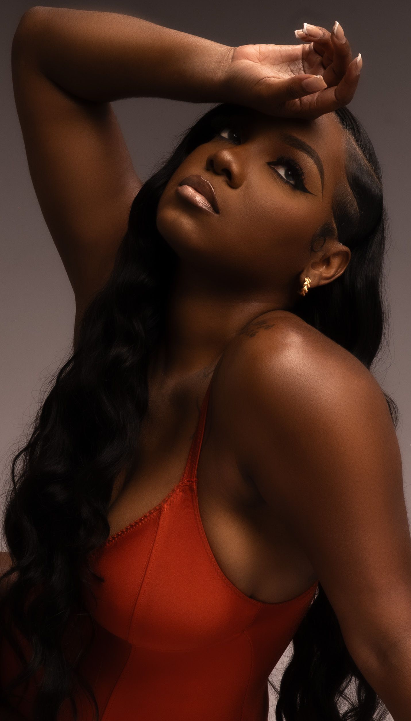 Dramatic beauty portrait in orange top with arm raised against brown background in Saint Petersburg Florida.