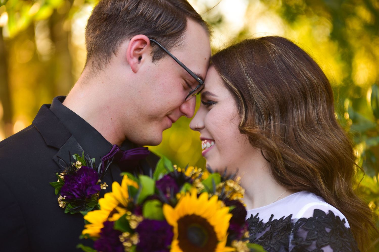 Couple sharing a romantic moment with sunflower and purple bouquet during fall outdoor engagement photo session.