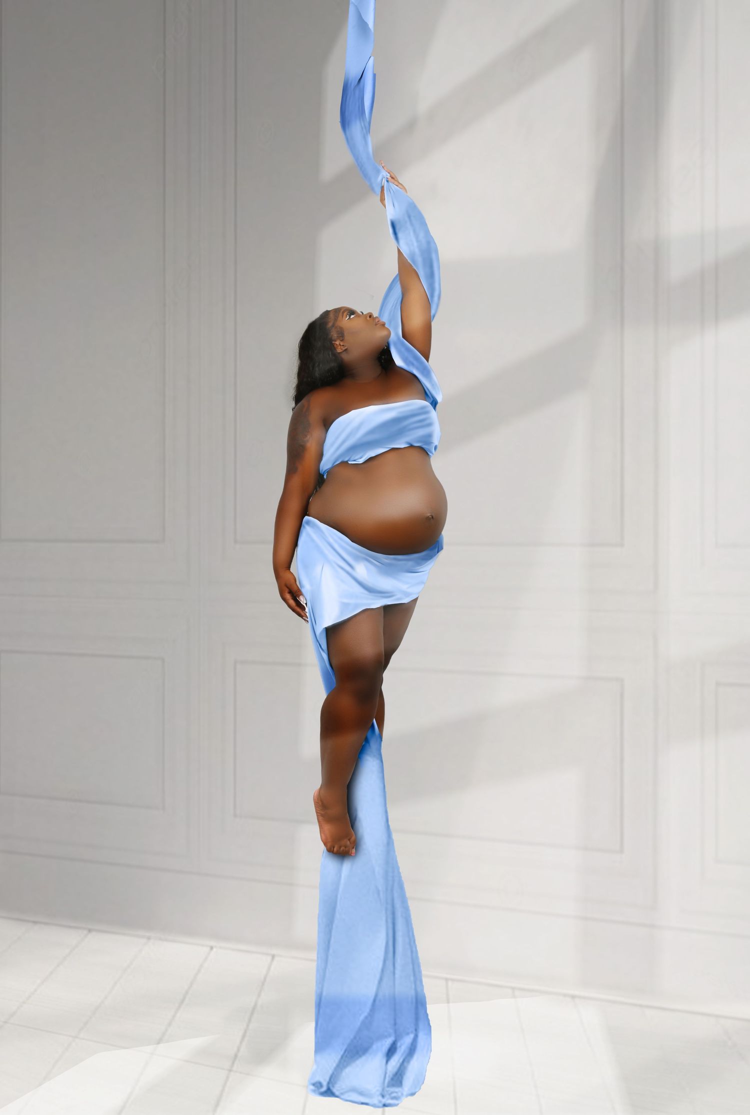 Maternity photoshoot featuring flowing light blue fabric in minimalist white setting.